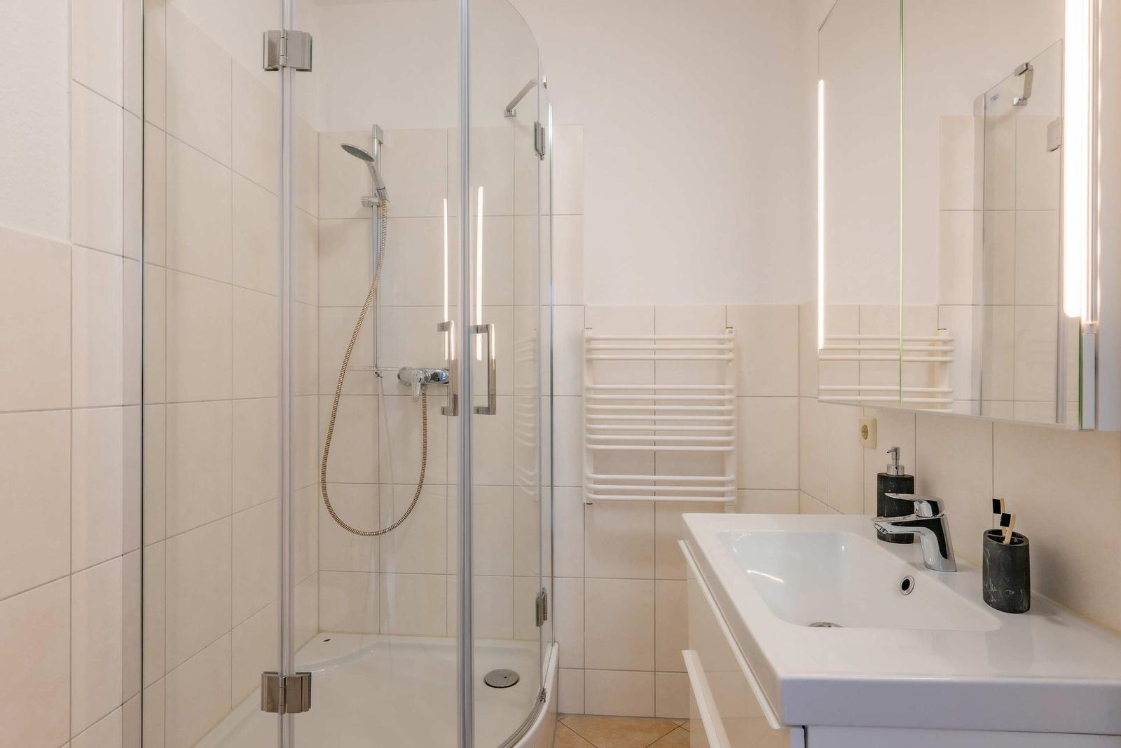 Badezimmer mit Dusche, Waschbecken und Heizkörper