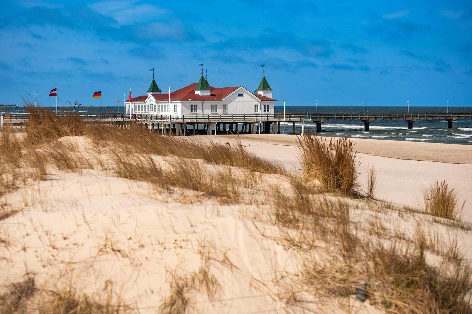 Weißes Haus auf Steg über Strand mit rotem Dach und grünen Türmen
