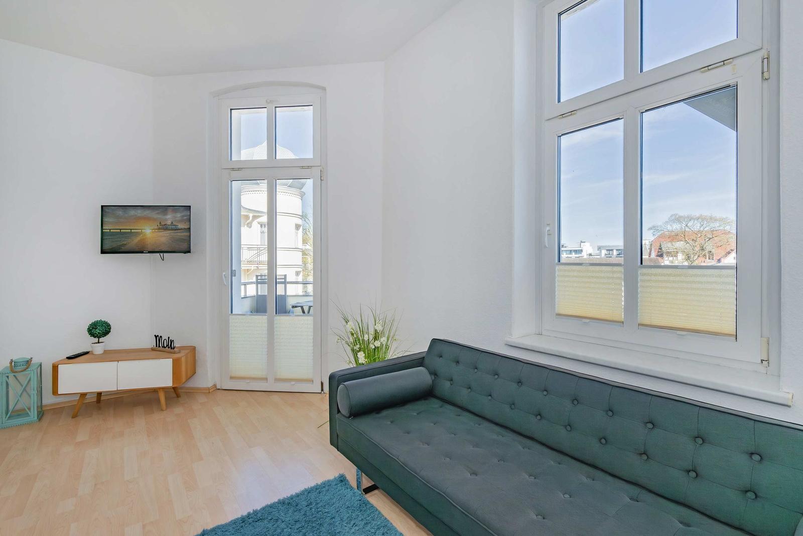 Wohnzimmer mit grünem Sofa, Fernseher und großen Fenstern mit Blick.
