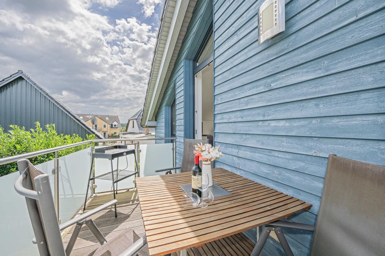 Terrasse mit Tisch, Stühlen, Grill und Blumen vor blauem Haus.