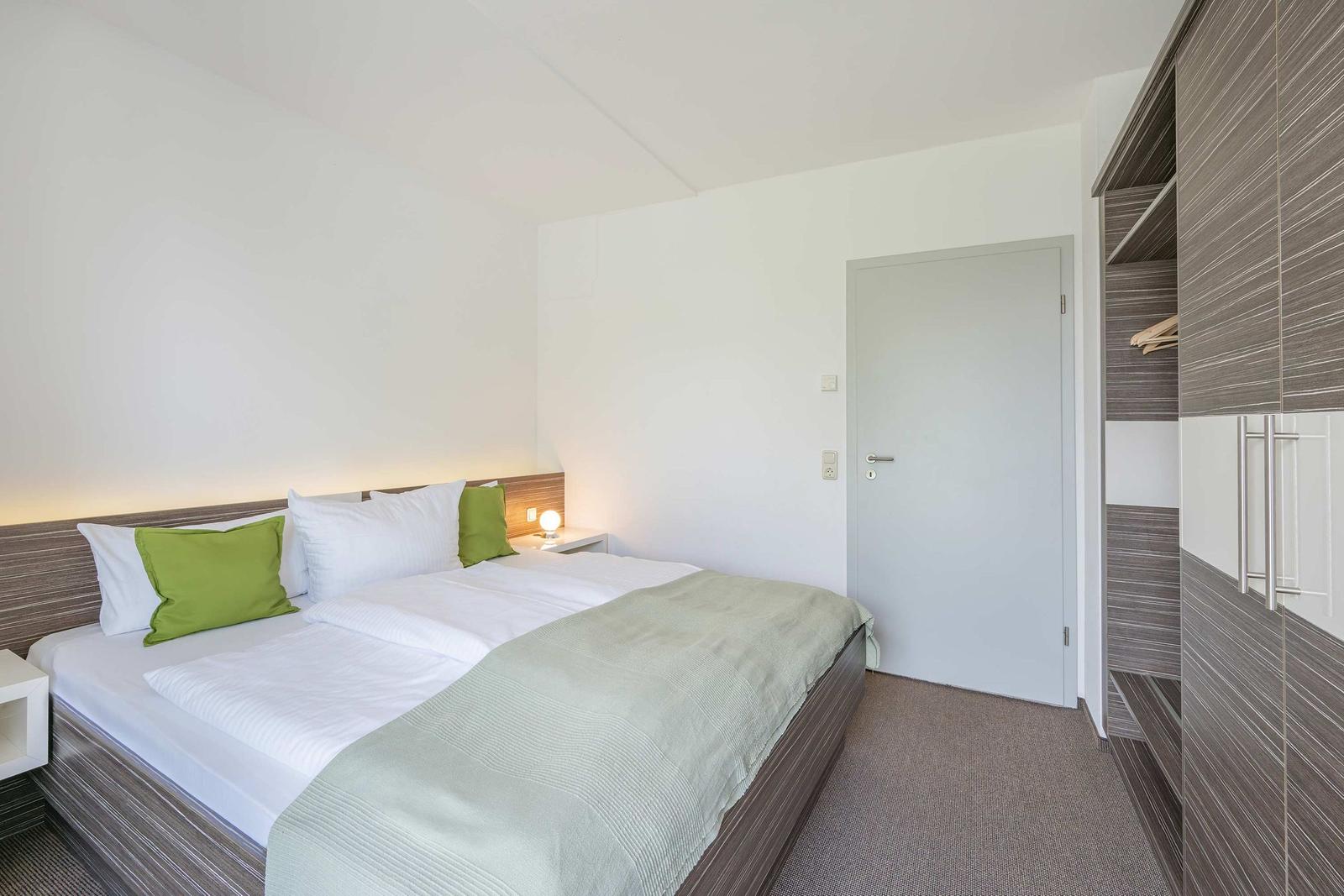 Schlafzimmer mit Doppelbett, grünen Kissen und Kleiderschrank