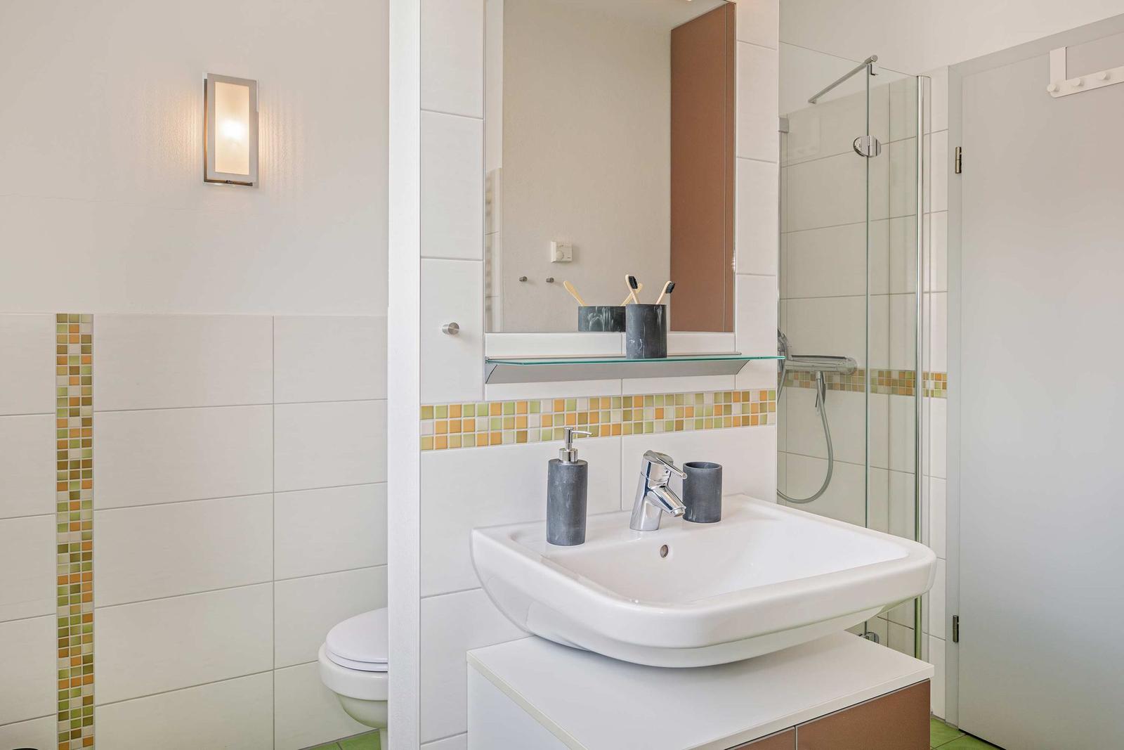Badezimmer mit Waschbecken, Dusche und Toilette. Wandfliesen mit Mosaikverzierung.