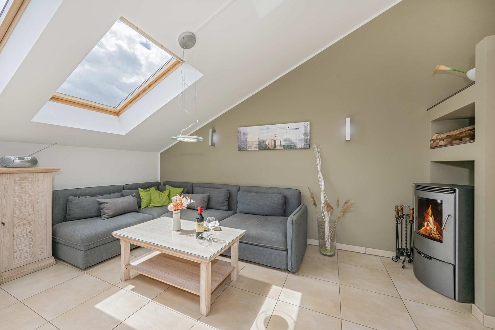 Wohnzimmer mit Sitzgruppe, Kamin und Dachfenster. Holztisch und Wandbild sichtbar.