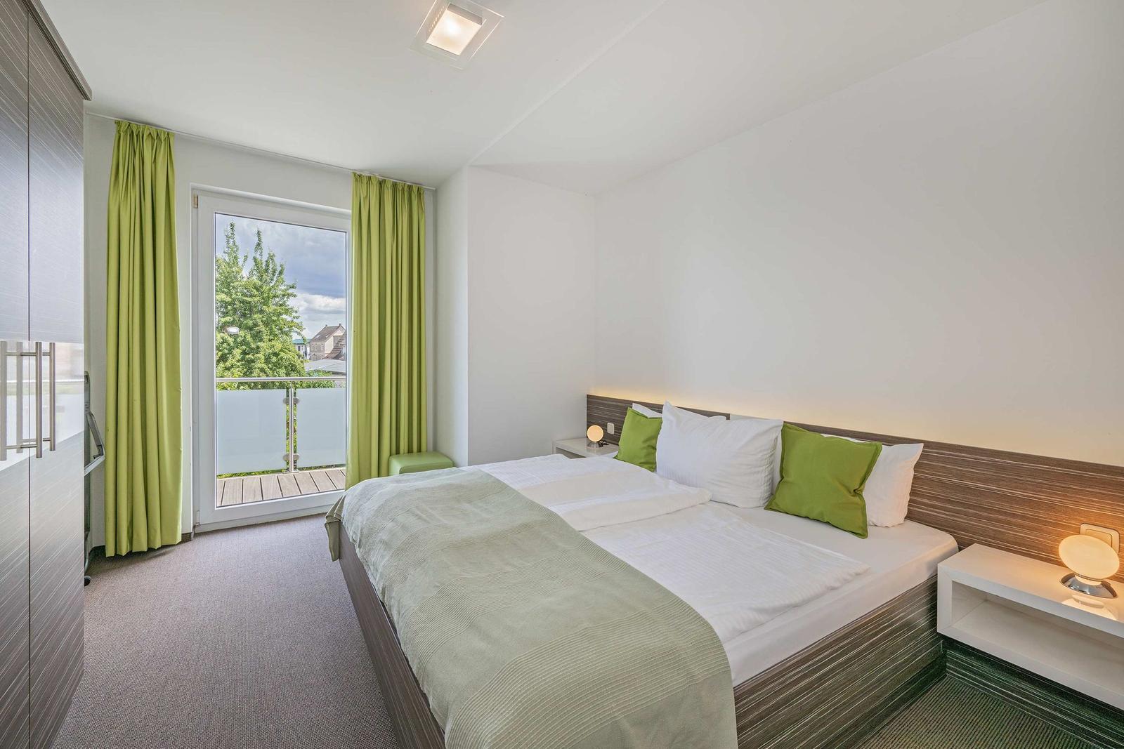 Schlafzimmer mit Bett, grünen Vorhängen und Balkonansicht.
