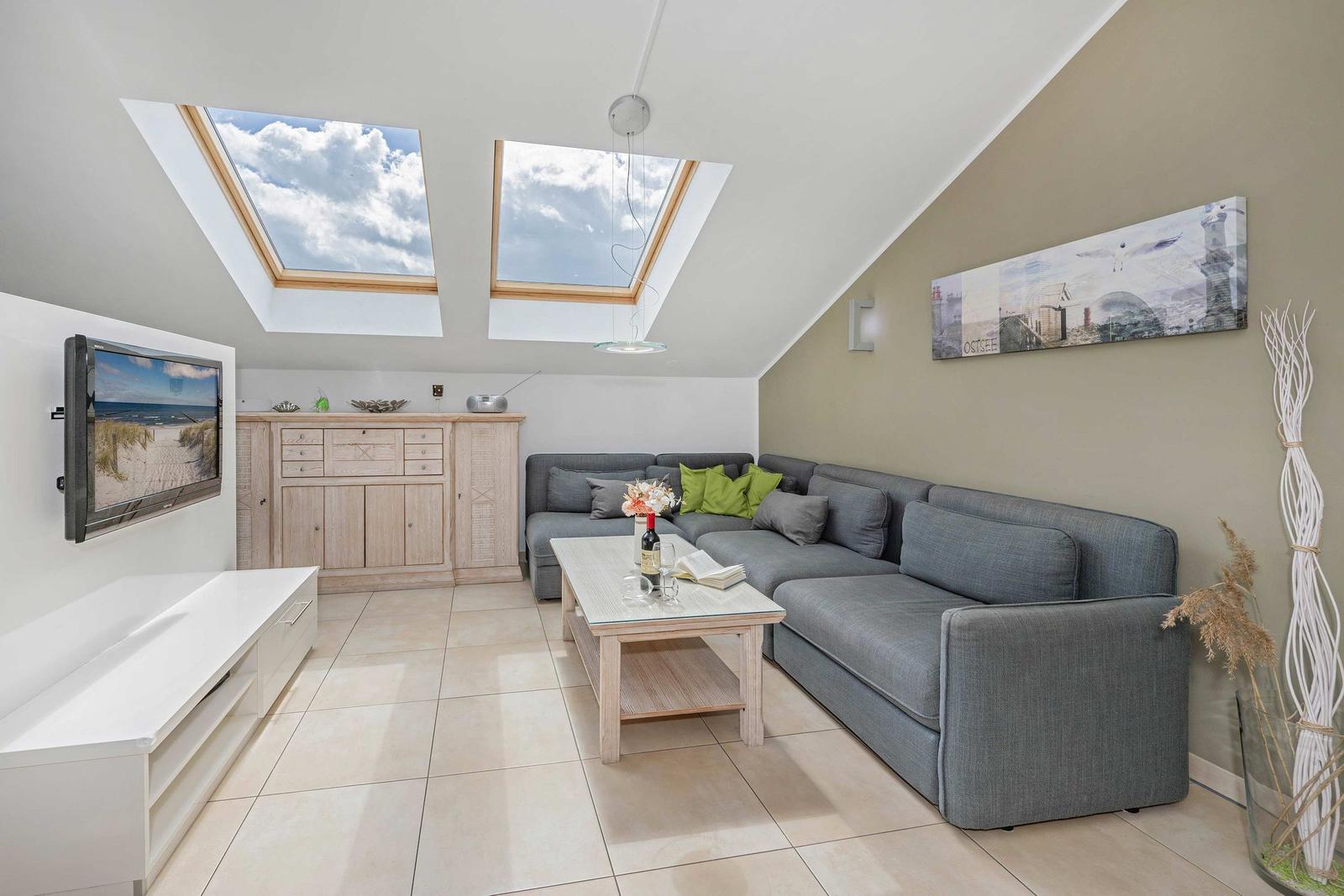 Wohnzimmer mit Dachfenstern, Sofa, Couchtisch und Fernseher an der Wand.