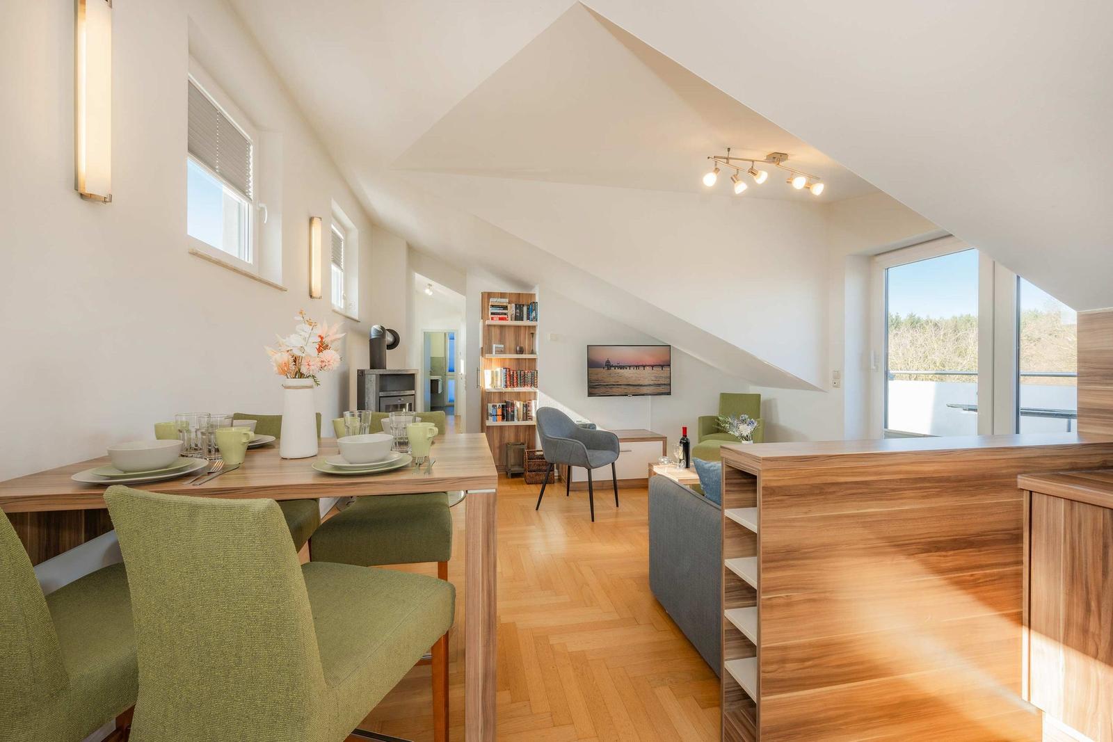 Essbereich mit Tisch und Stühlen, Wohnbereich mit Sofa und Fernseher, Holzboden und große Fenster.