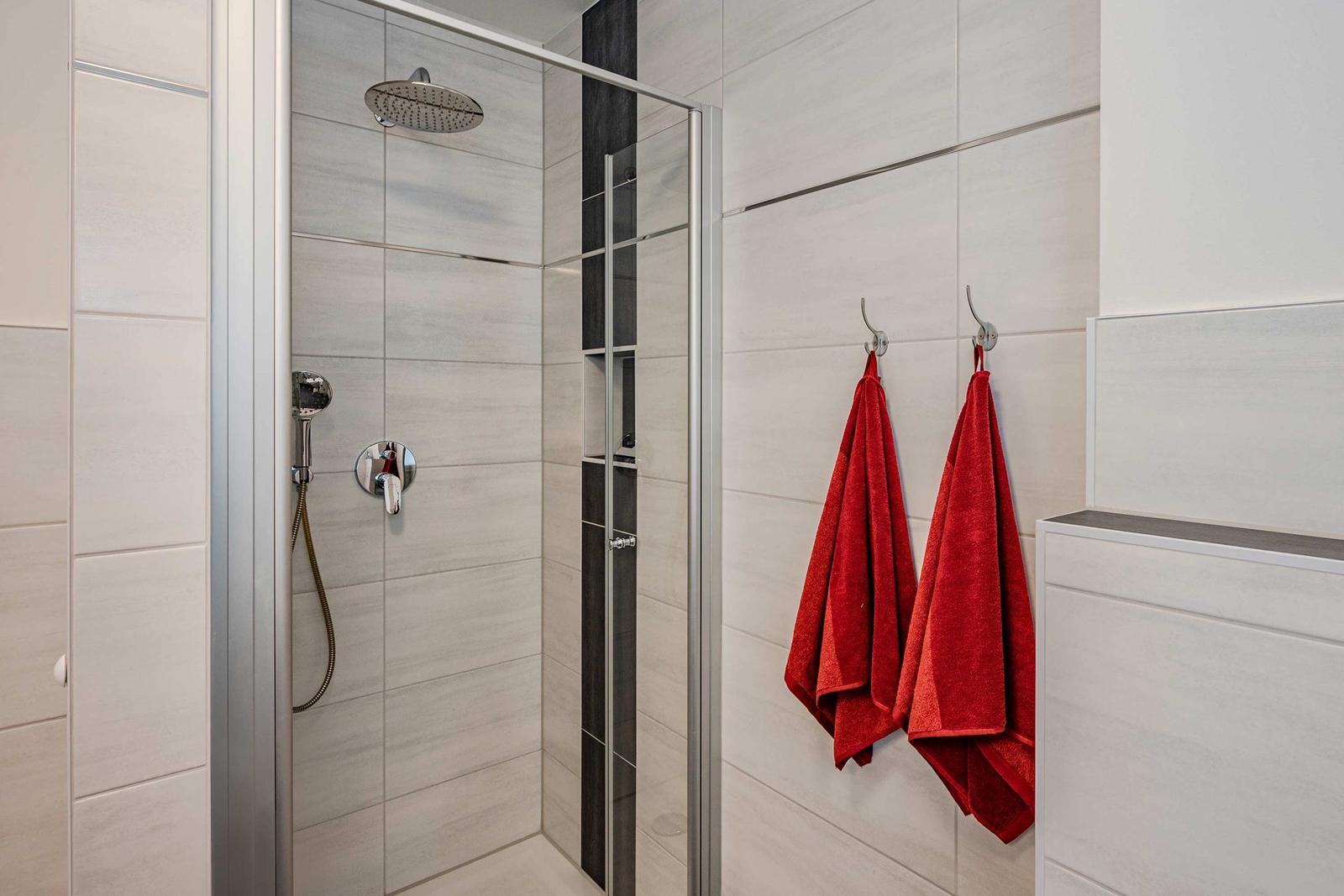 Dusche mit Glaswand, roten Handtüchern und hellen Fliesen.