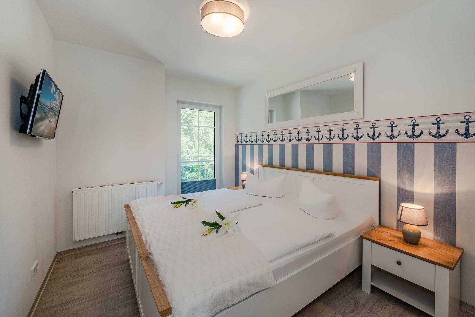 Schlafzimmer mit Bett, Nachttisch, Fernseher und Fenster mit Blick.