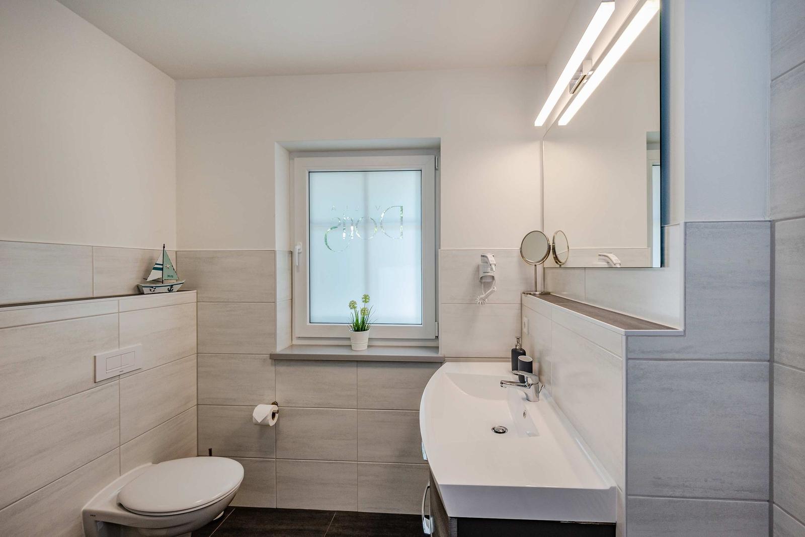 Badezimmer mit Toilette, Waschbecken und Fenster mit Pflanze.