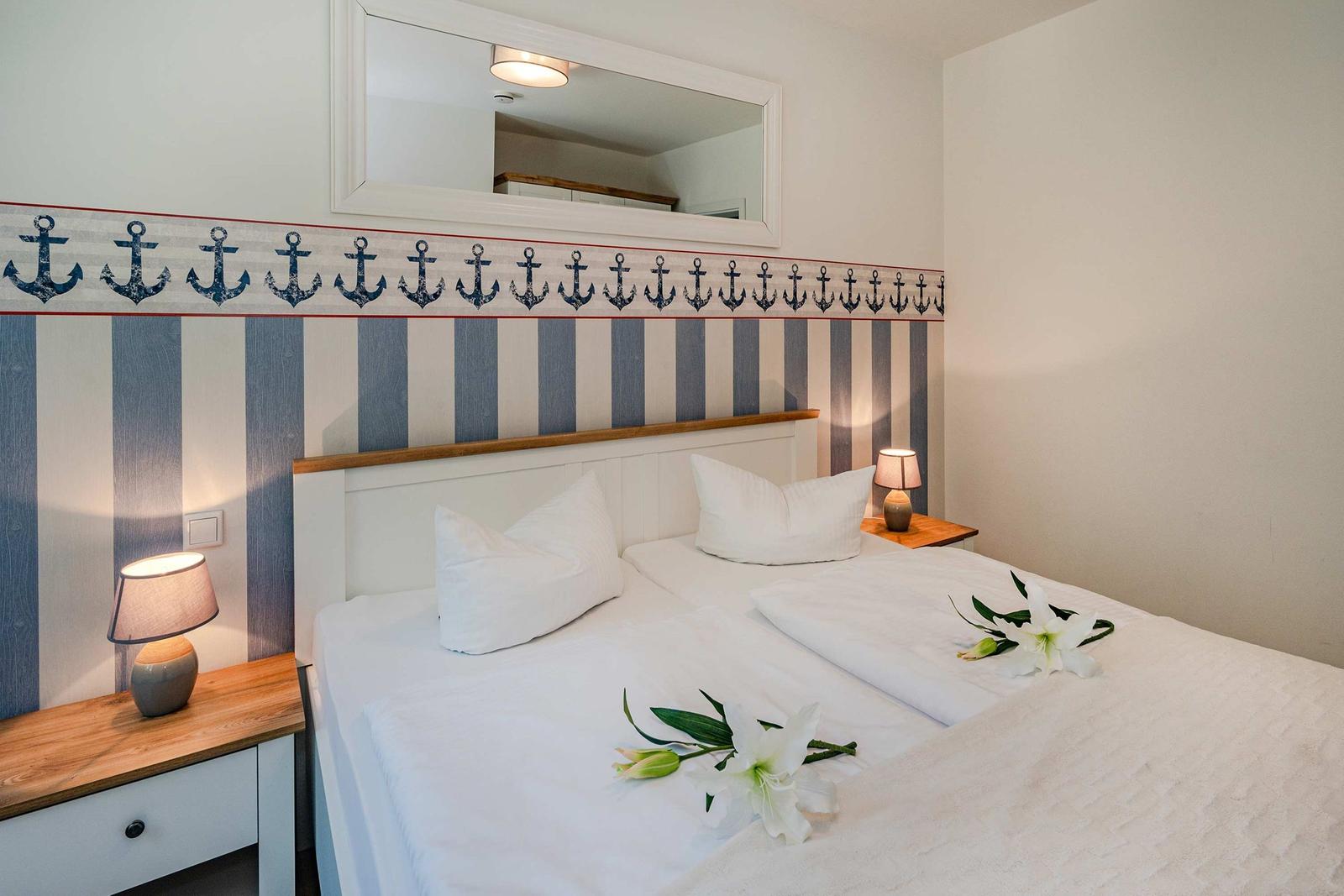Schlafzimmer mit Bett, Nachttischen und Wandtapete mit Ankern.