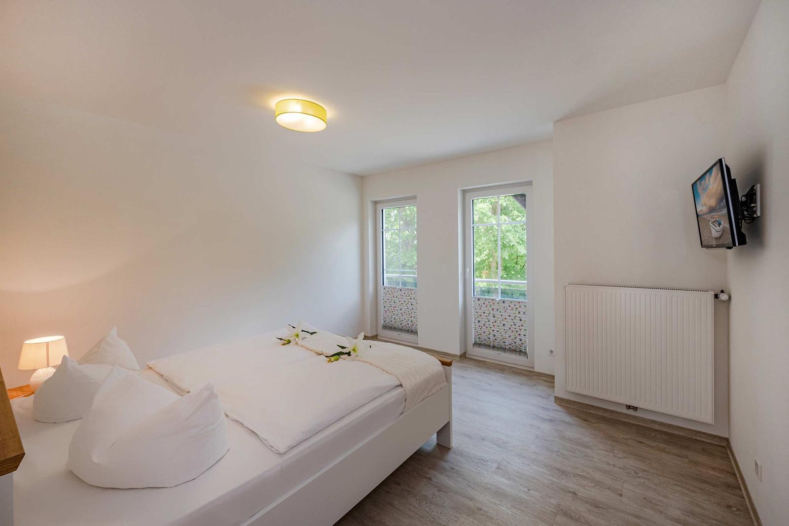 Schlafzimmer mit Doppelbett, Fenstern und TV-Wandmontage.