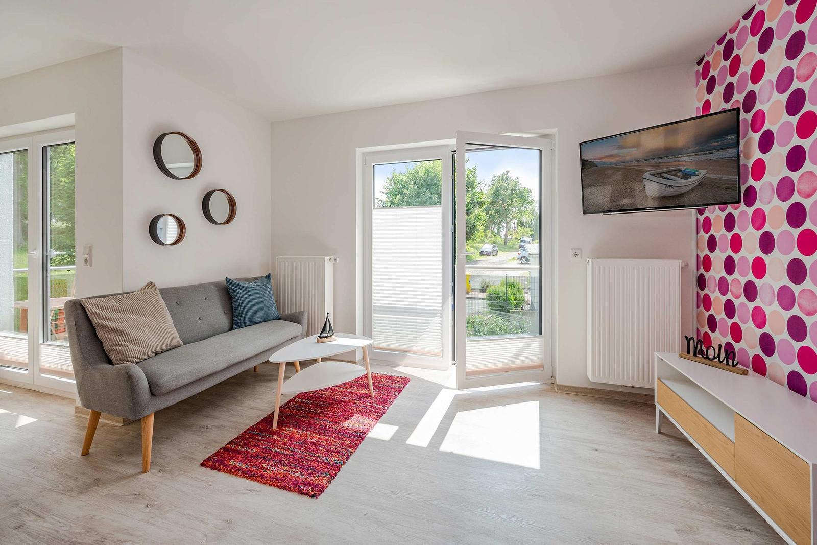 Wohnzimmer mit Sofa, TV und Terrassentür. Wand mit buntem Muster.