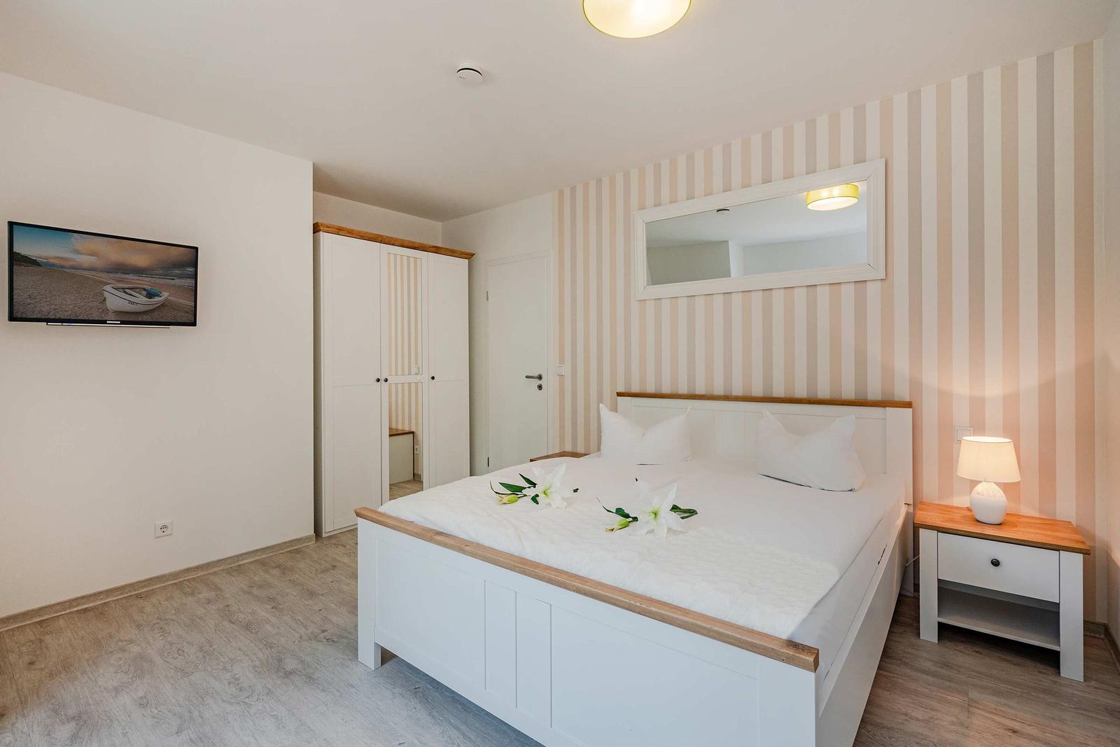 Schlafzimmer mit Bett, Nachttisch, Spiegel und TV an der Wand.