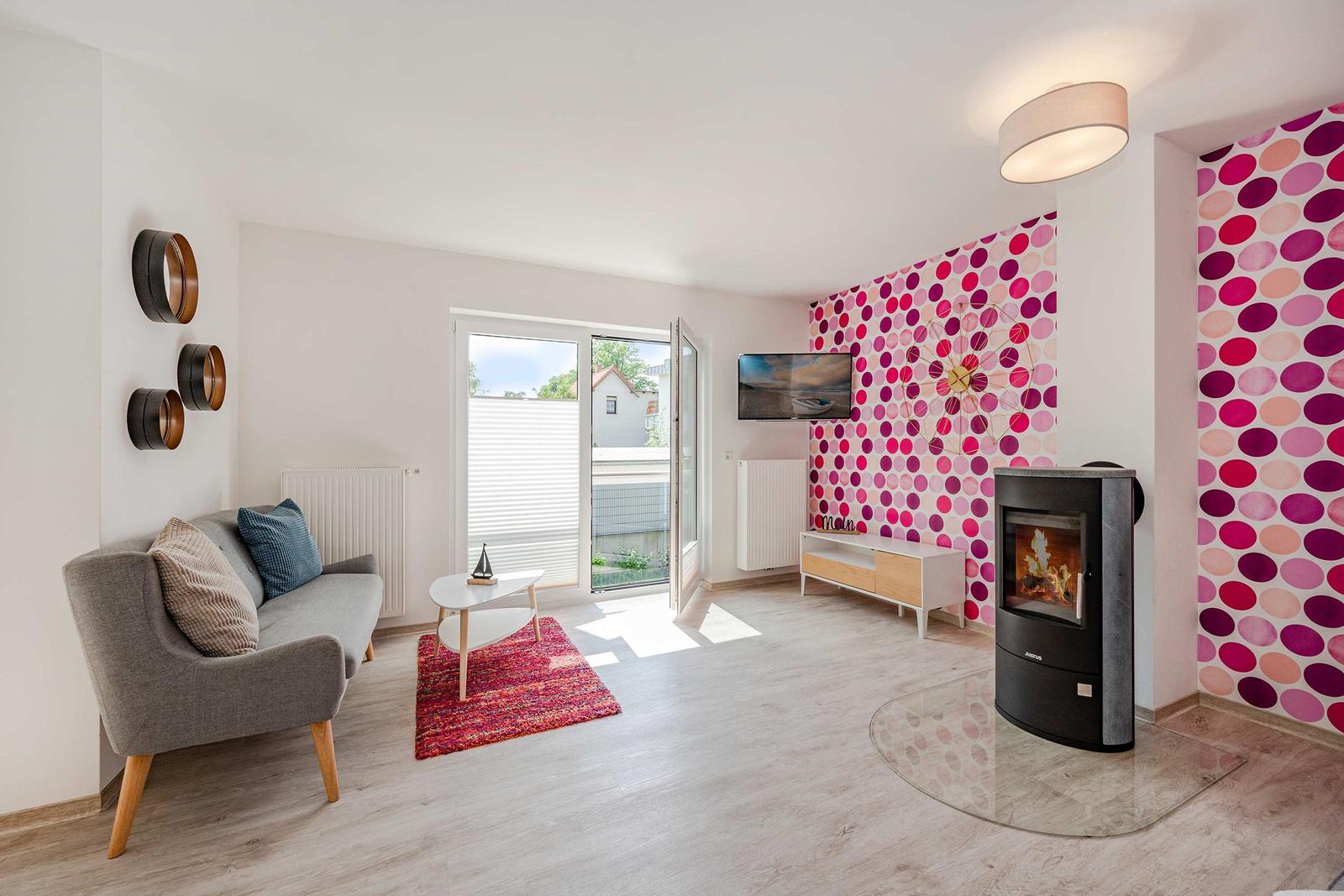 Wohnzimmer mit Sofa, Kamin und farbiger Wand. Tür führt auf Balkon.