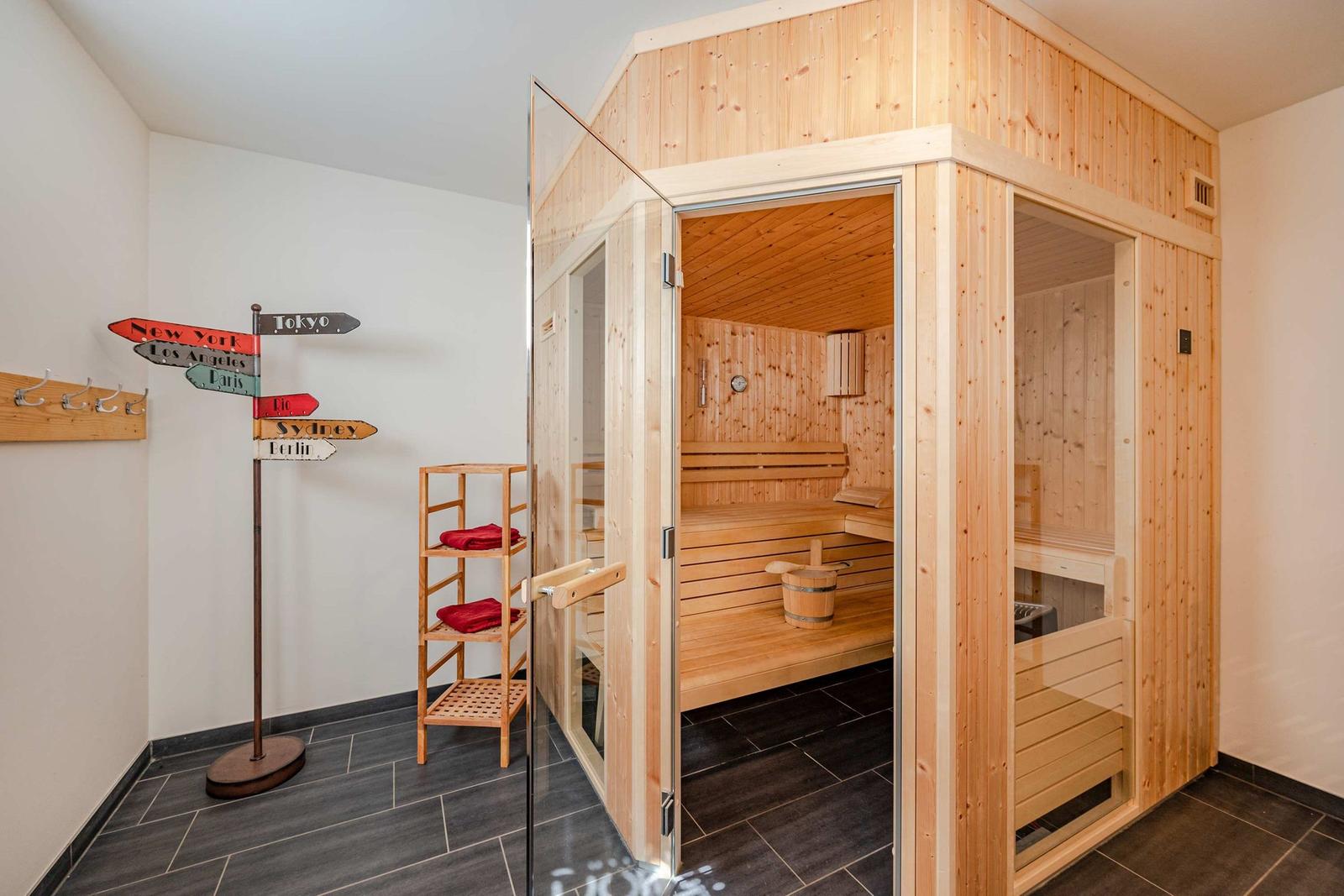 Sauna mit Holzverkleidung und Sitzbänken. Nebenraum mit Ständer und Wegweiser.