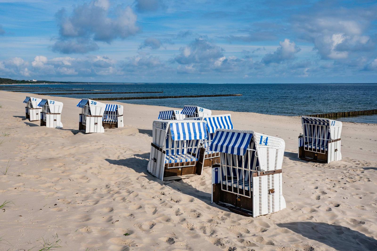 Strand mit weißen Strandkörben und blau-weißem Streifenmuster, Blick auf das Meer.