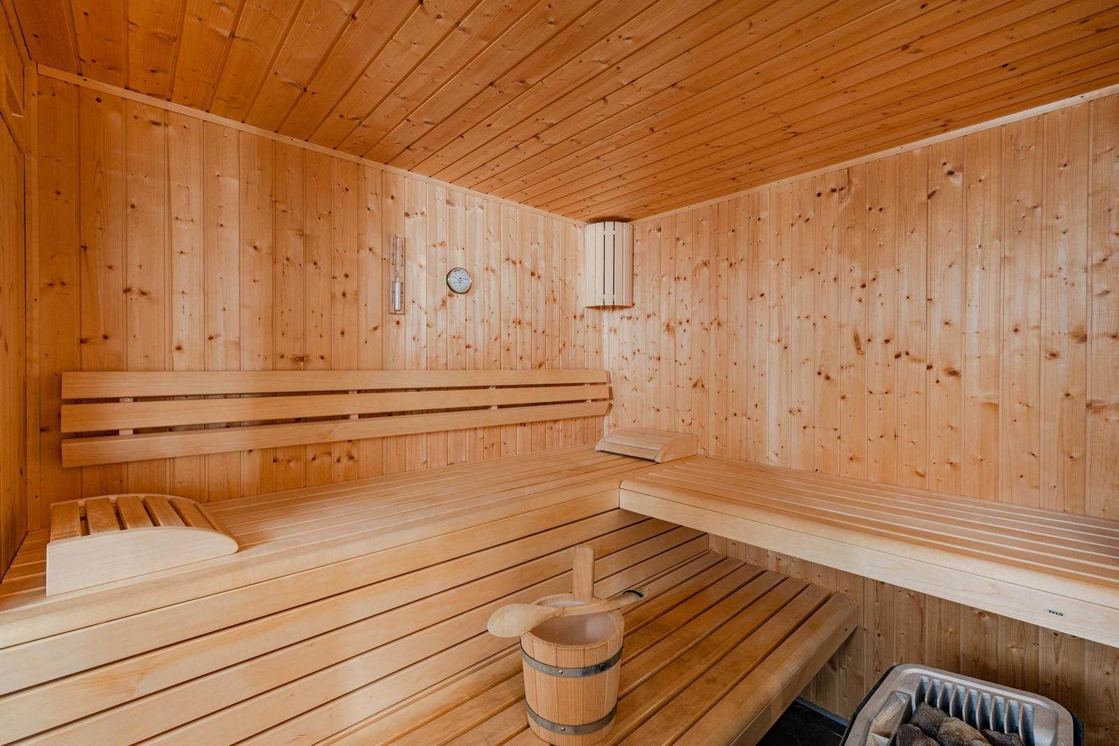 Holzsauna mit Sitzbänken, Körbchen und Thermometer an der Wand.