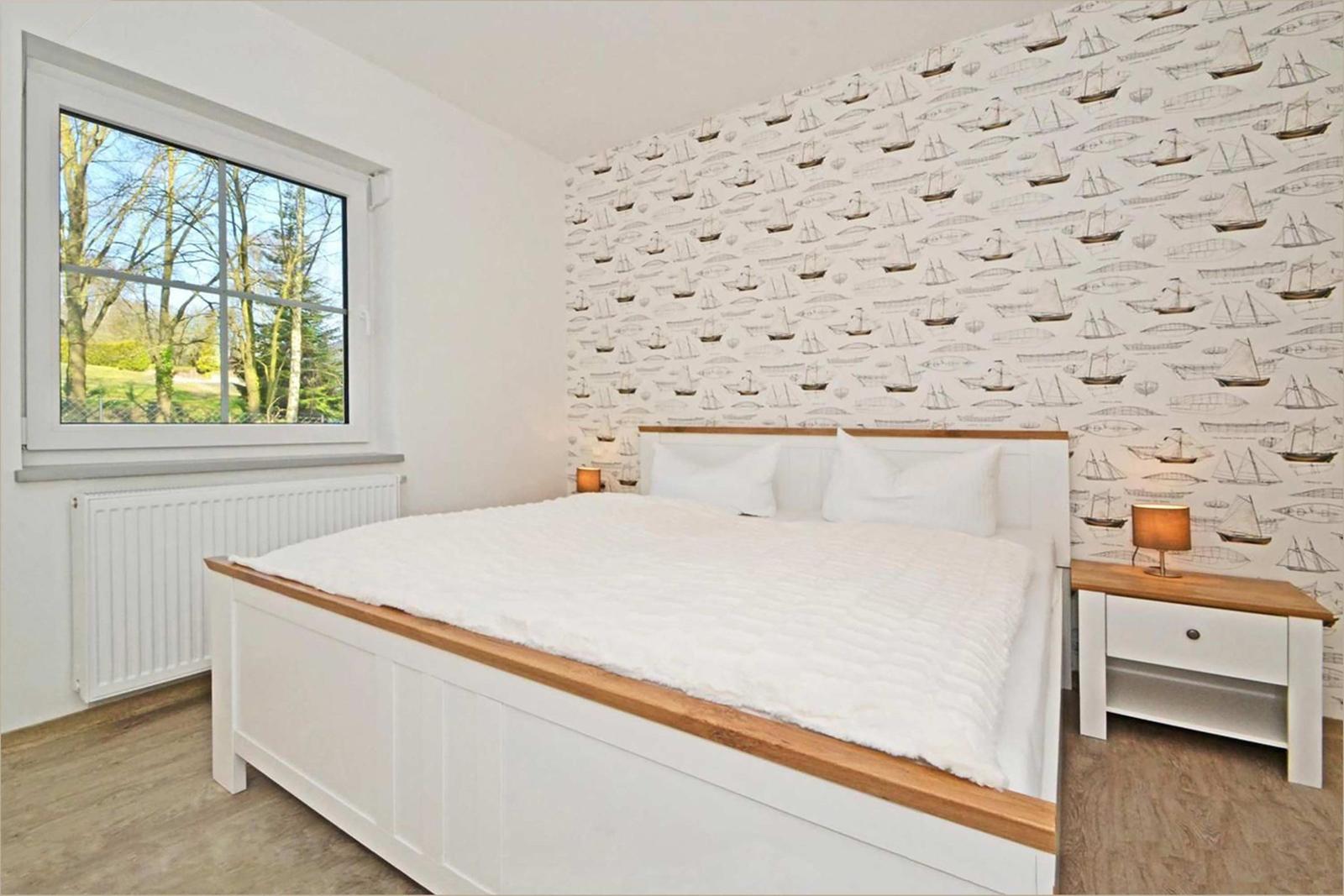 Schlafzimmer mit Bett, Nachttisch und Fenster mit Blick auf Garten.