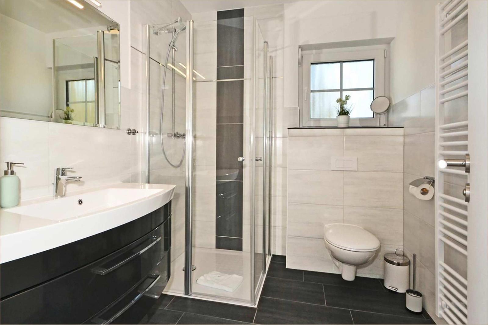Badezimmer mit Dusche, Waschbecken und Toilette. Fenster mit Pflanze.