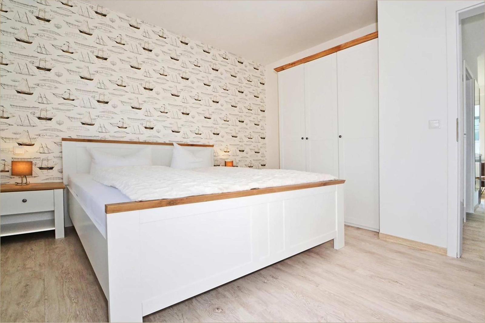 Schlafzimmer mit Bett, Schrank und Tapete mit Schiffsmotiven.