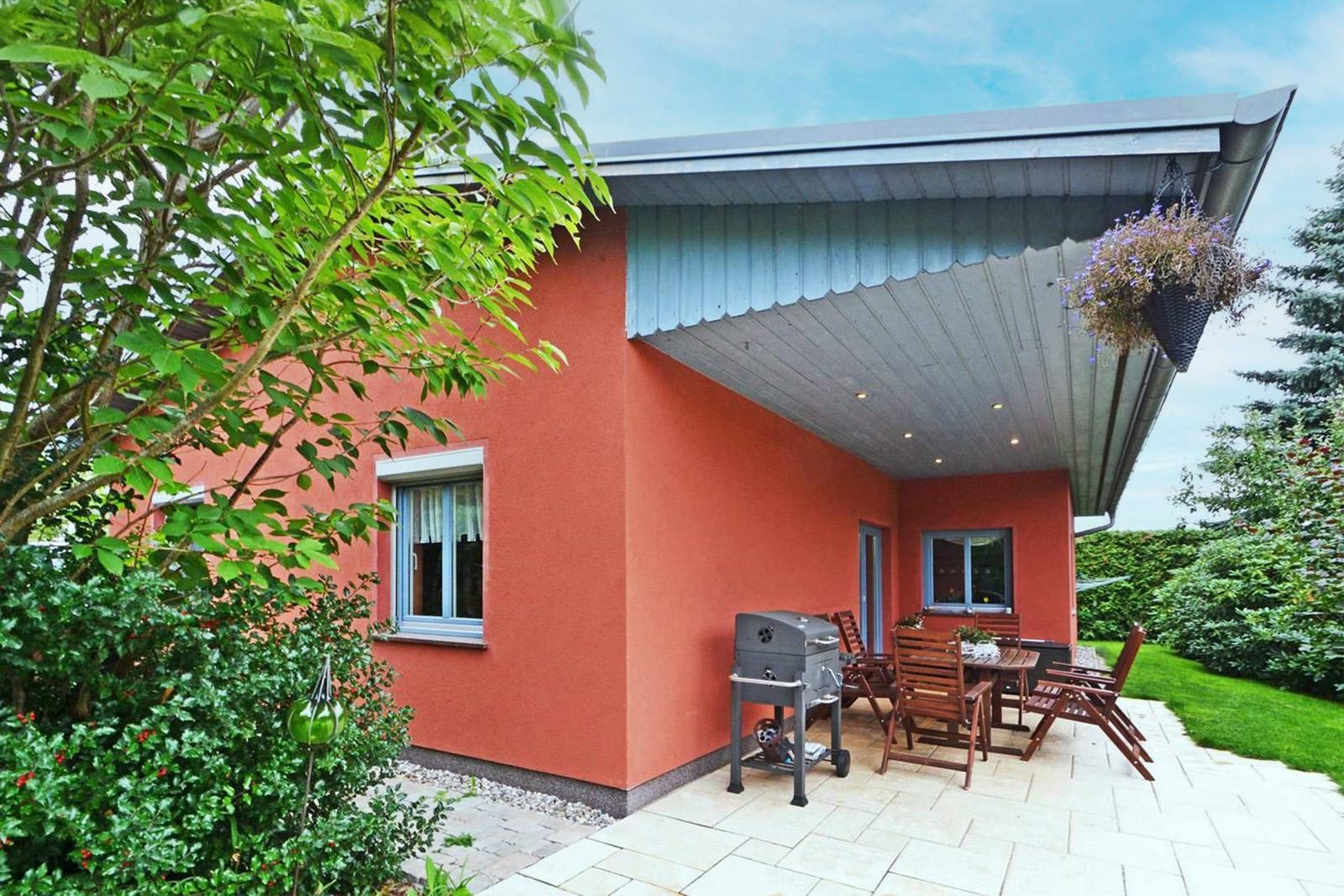 Rotes Haus mit überdachter Terrasse, Grill und Holzmöbeln im Garten.
