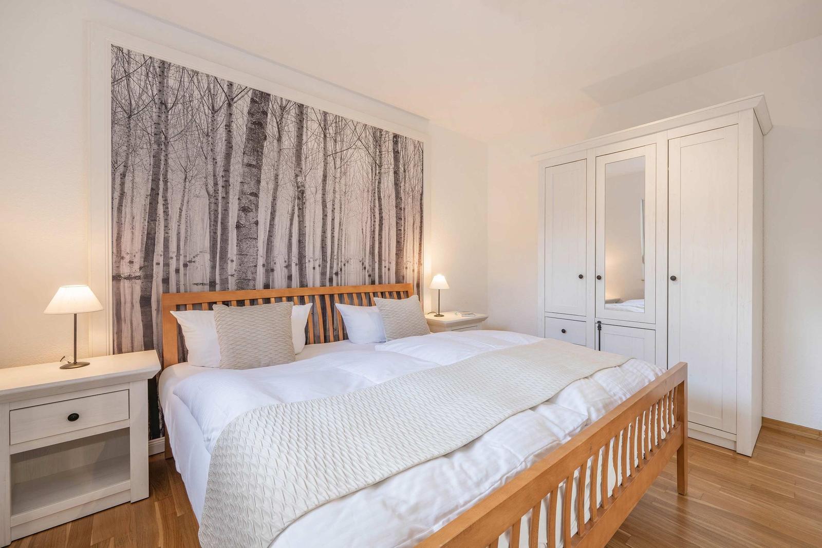 Bedroom with bed, nightstands, and wardrobe. Wallpaper shows trees.