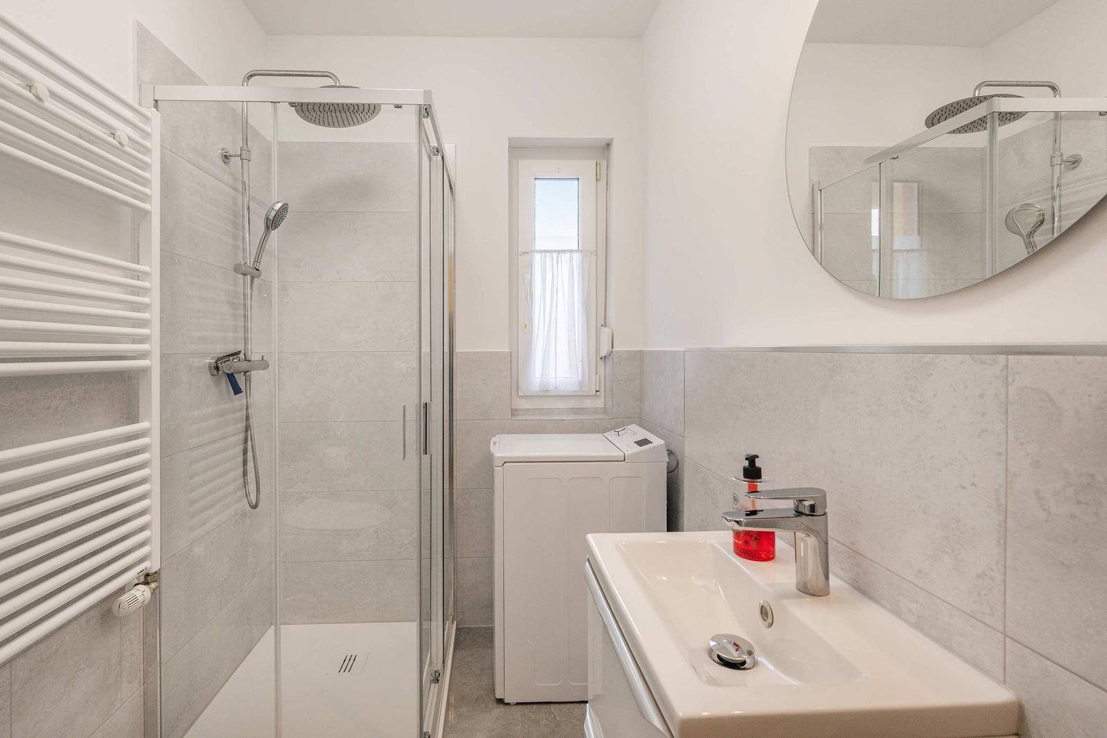 Bathroom with shower, washing machine, and sink with mirror.