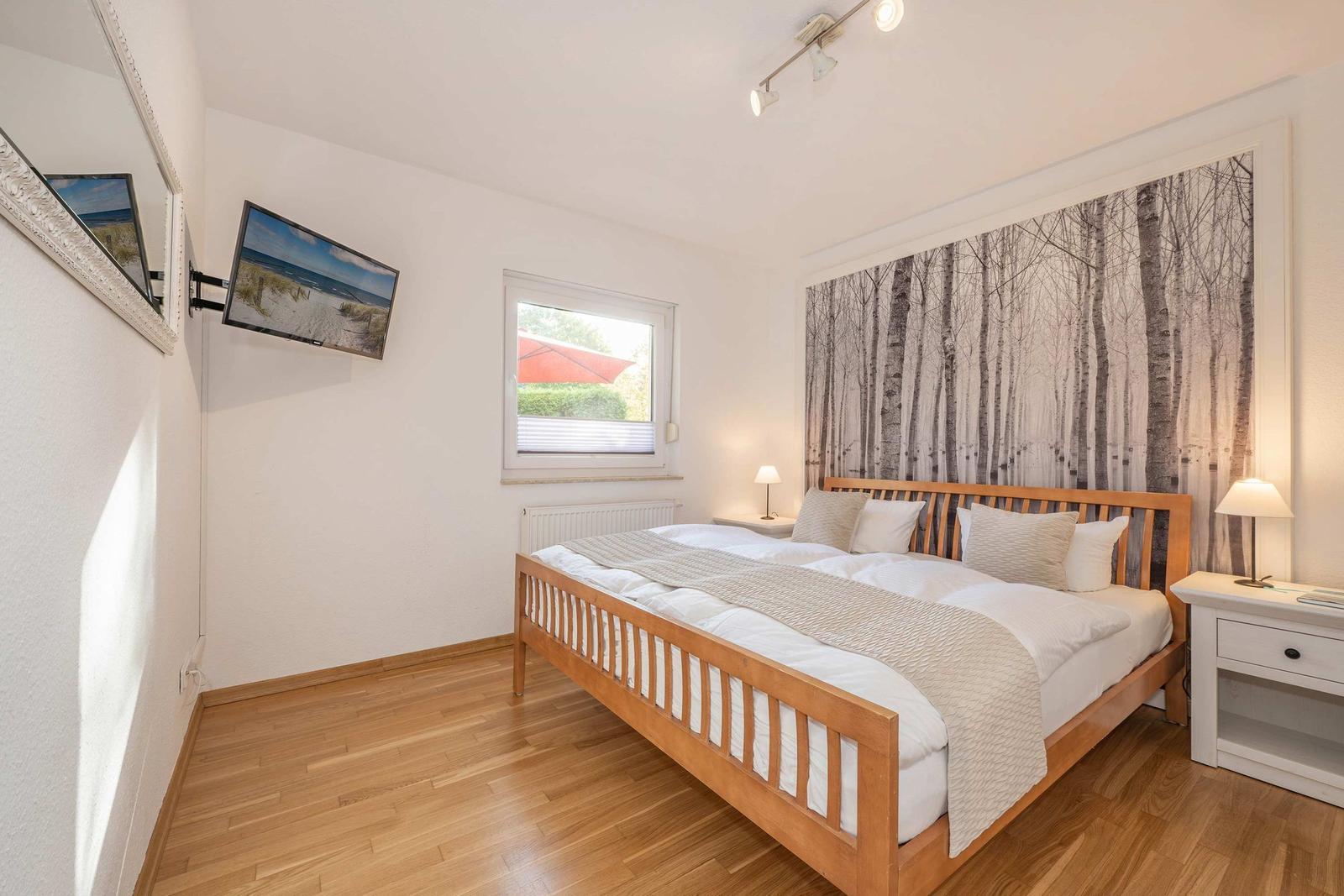 Bedroom with wooden bed, wall art, and TV mounted on the wall.