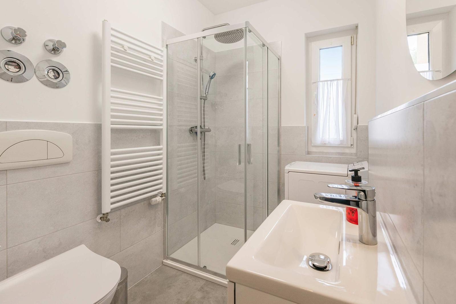 Bathroom with shower, sink, and toilet. Window with curtain.