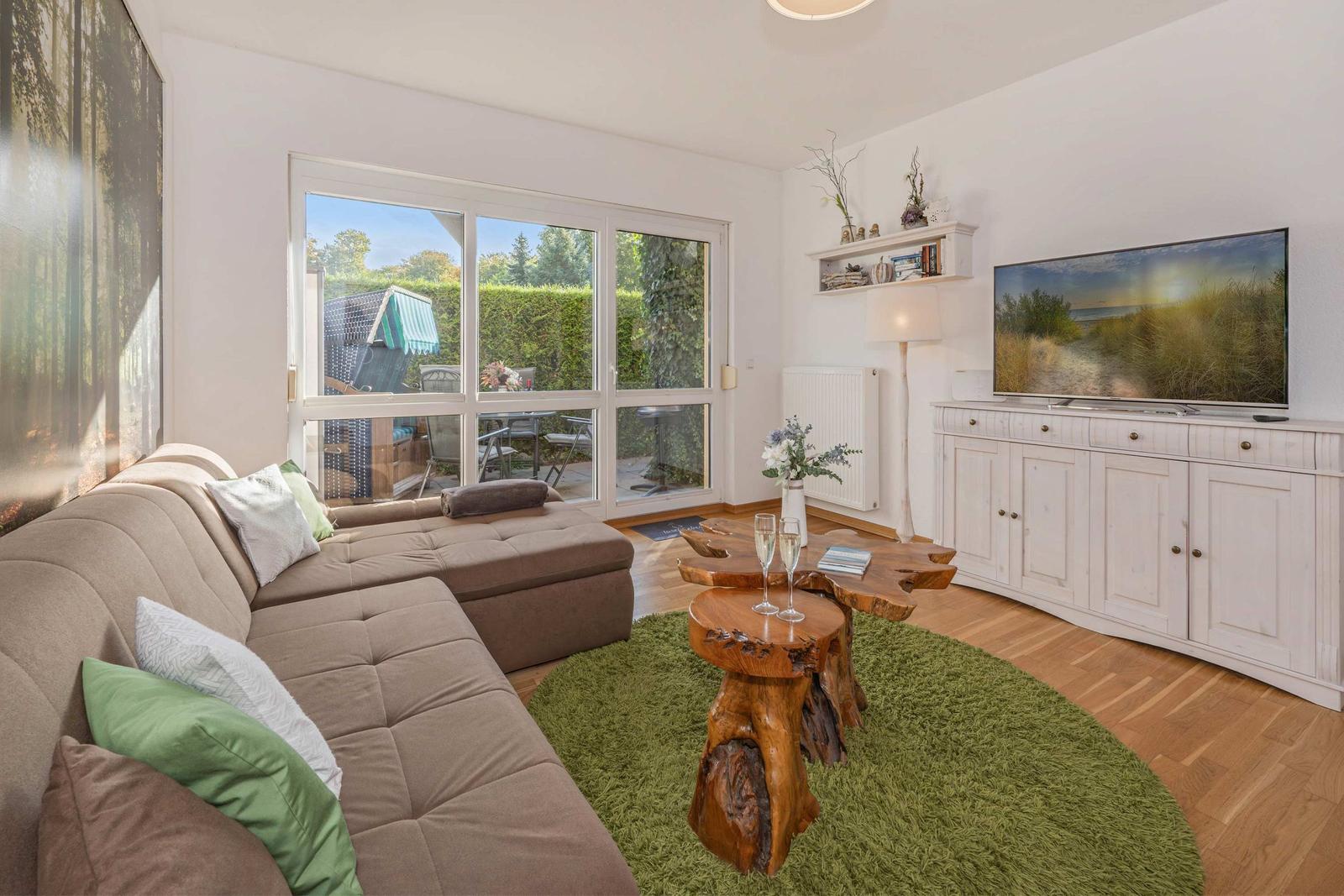 Living room with sofa, wooden table, and TV. Entrance to terrace with garden.