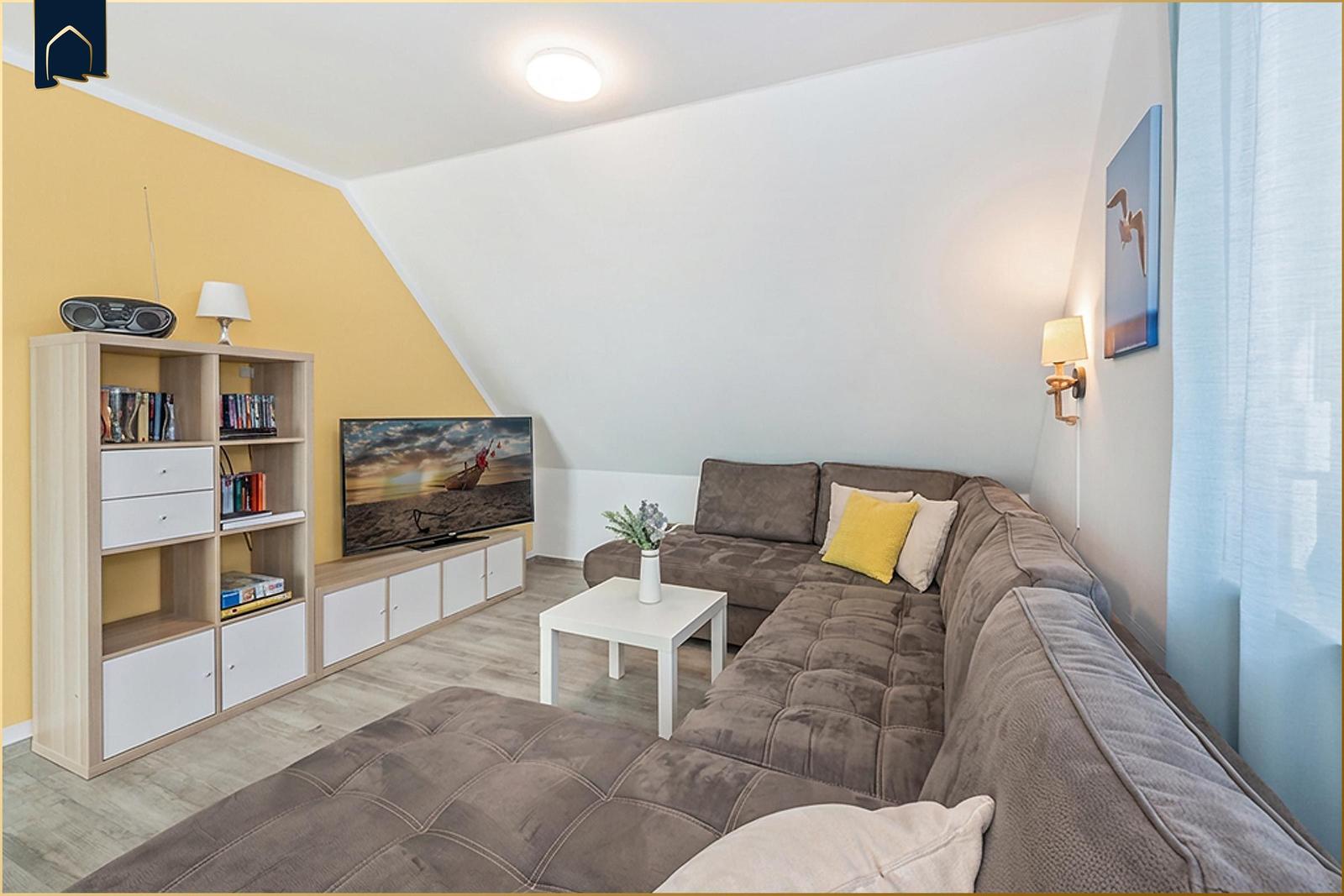 Wohnzimmer mit Sofa, Fernseher und Bücherregal an gelber Wand.