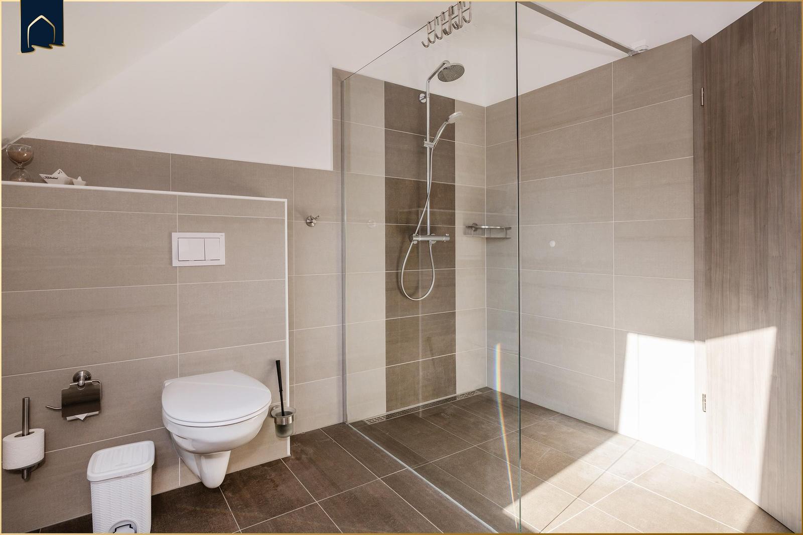 Bad mit Dusche, Toilette und Toilettenpapierhalter an der Wand.