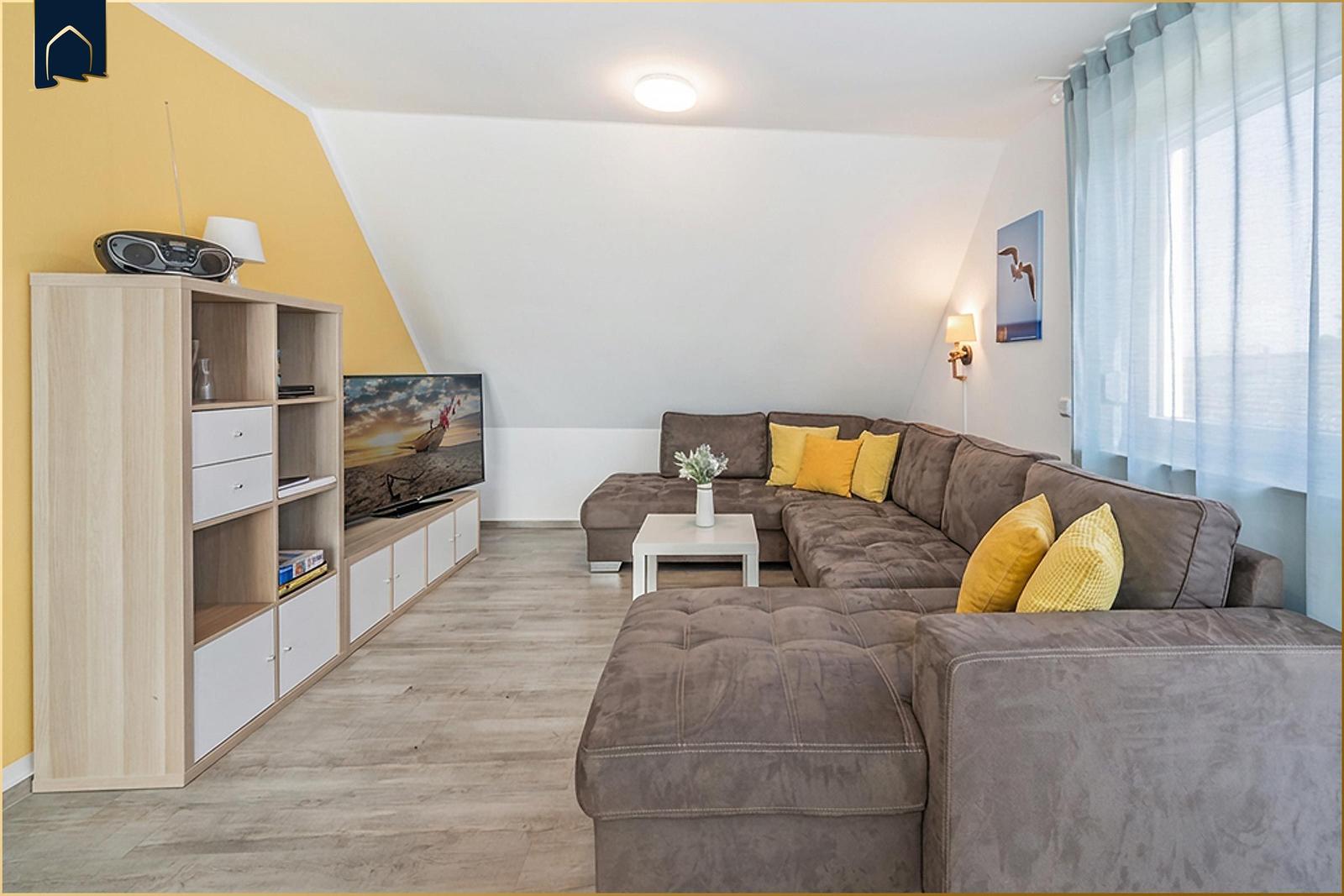 Ein Wohnzimmer mit braunem Sofa, gelben Kissen und einem Fernseher auf einem Schrank.