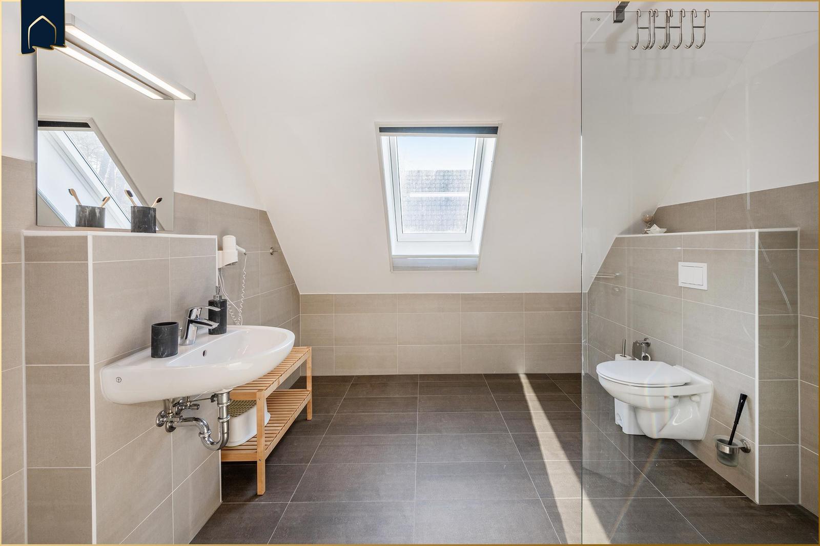 Badezimmer mit Dusche, Toilette und Waschbecken unter Dachschrägen.