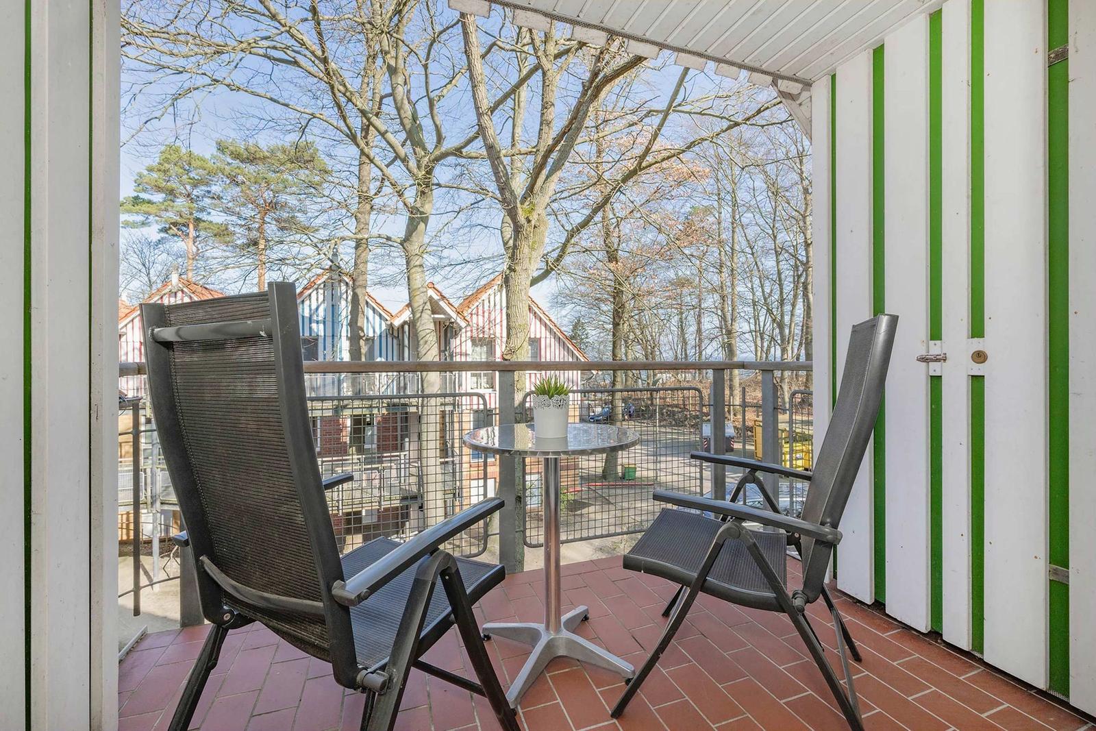 Terrasse mit zwei Stühlen und Tisch, Blick auf Bäume und Häuser.