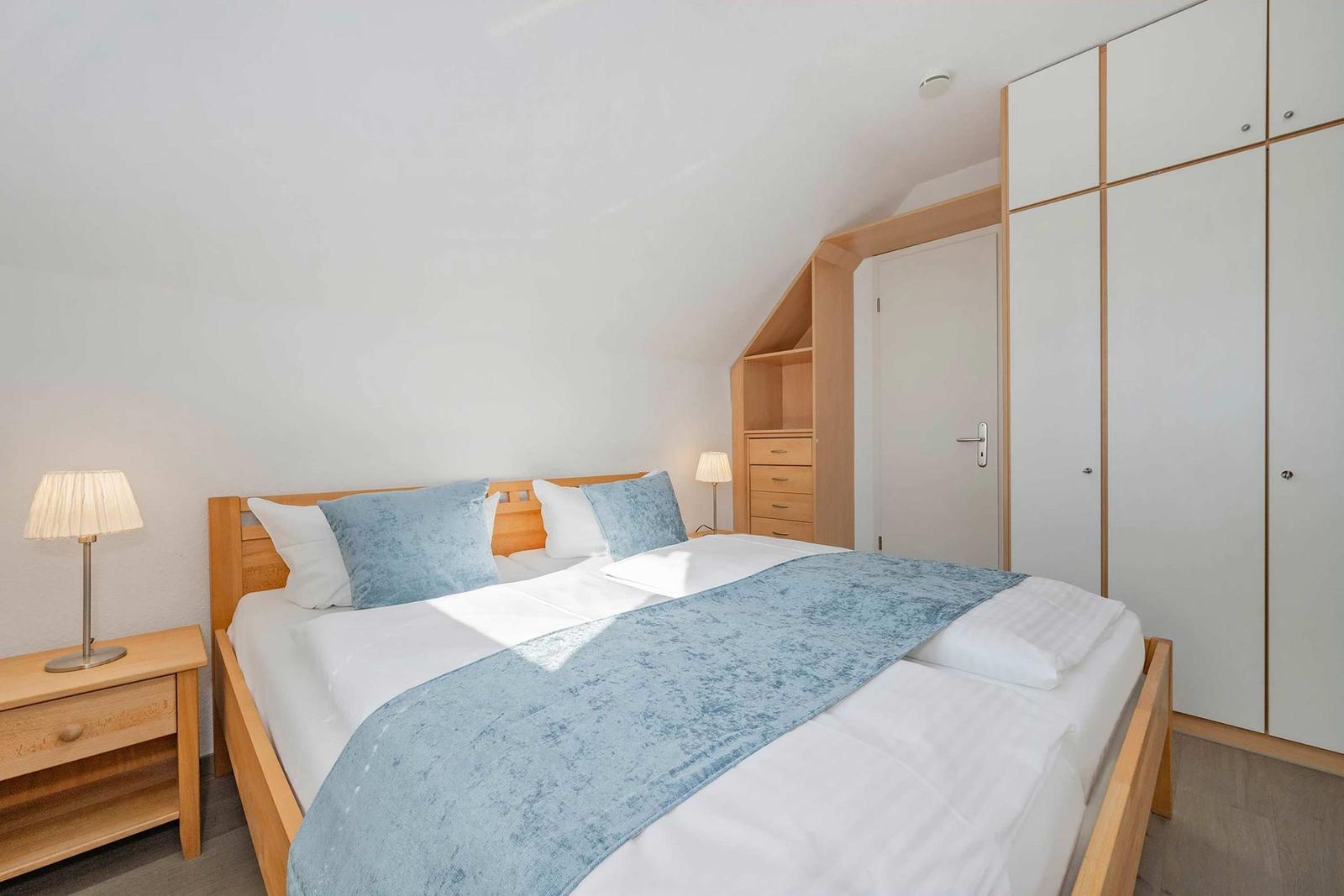 Schlafzimmer mit Bett, Nachttisch und Kleiderschrank. Dachschrägen und Holzmöbel.