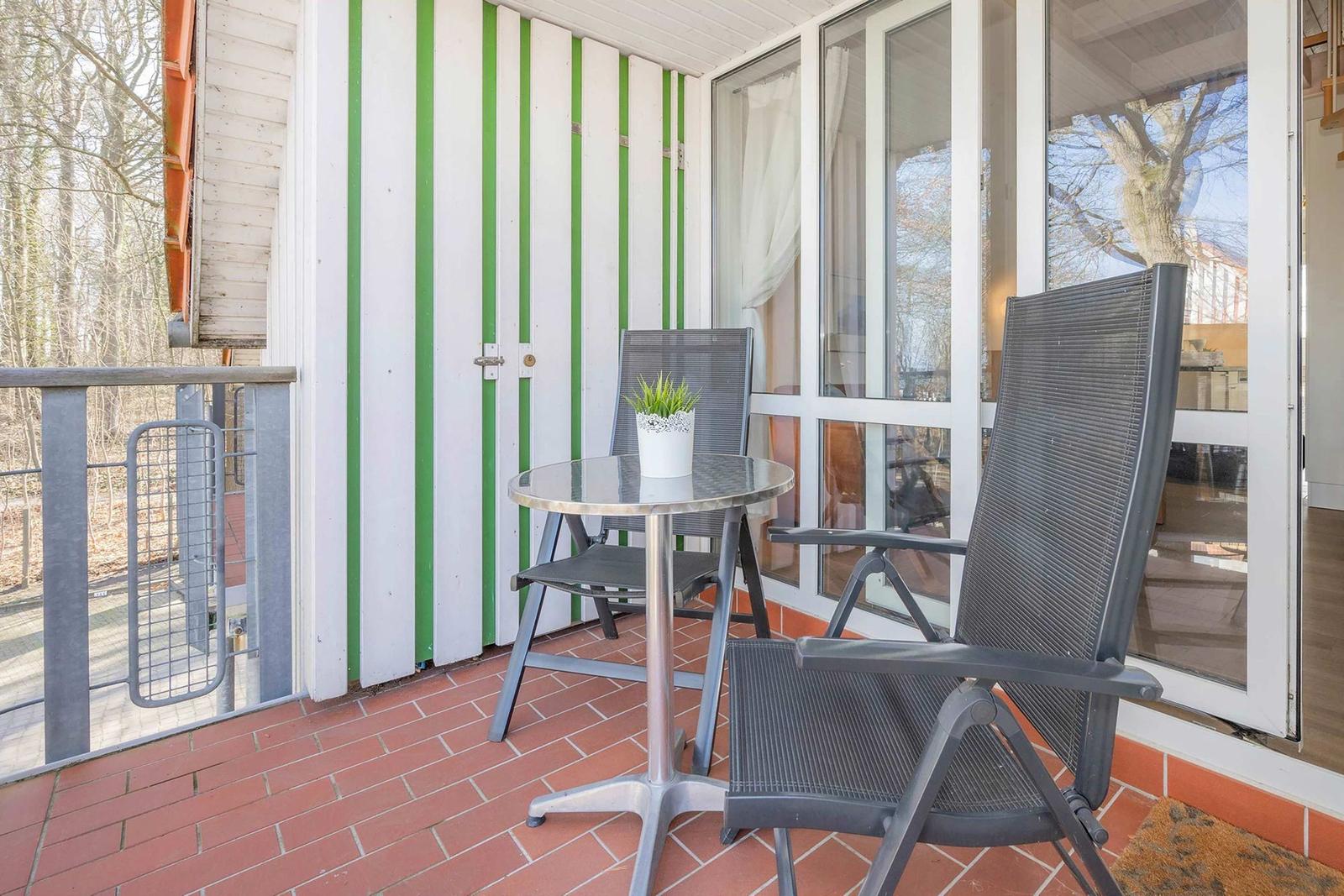 Terrasse mit Tisch und zwei Stühlen, grün-weiße Wand, Glasfenster, roter Fliesenboden.