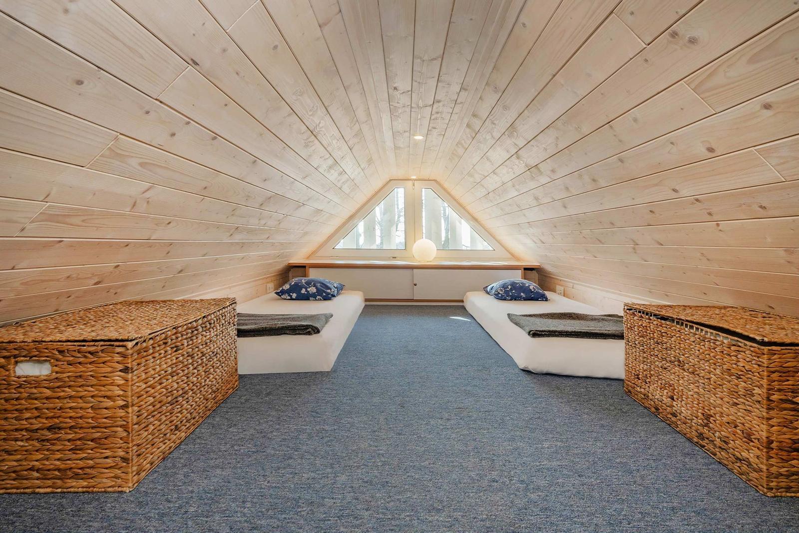 Zimmer mit zwei Matratzen, Holzwänden und Dachfenster. Zwei Körbe stehen an den Seiten.