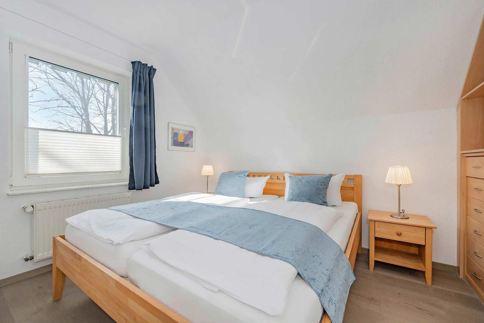 Ein Schlafzimmer mit Doppelbett, Holzmöbeln und Fenster mit Blick auf Bäume.