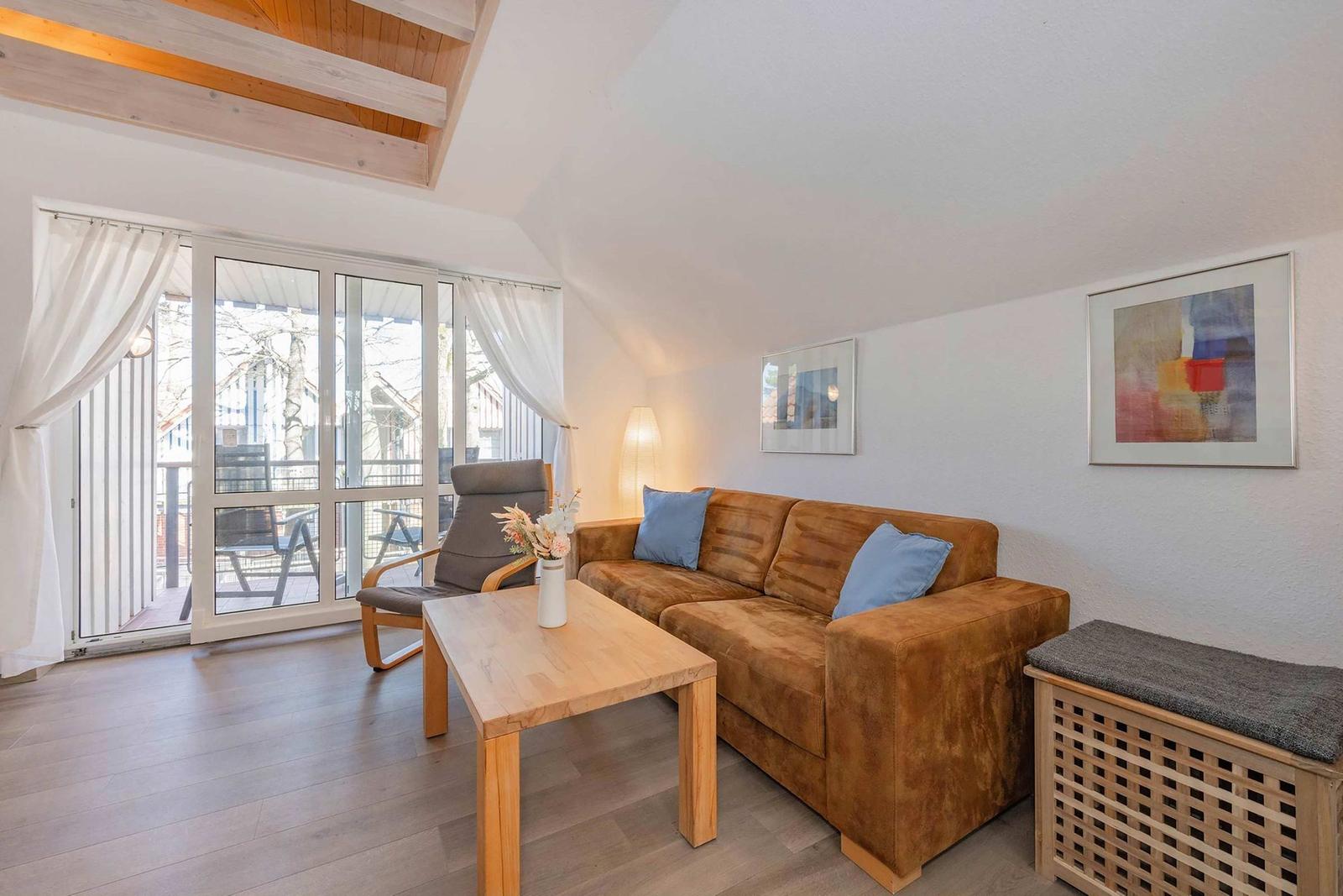 Wohnzimmer mit Sofa, Tisch und Balkontür. Holzdecke und Bilder an der Wand.