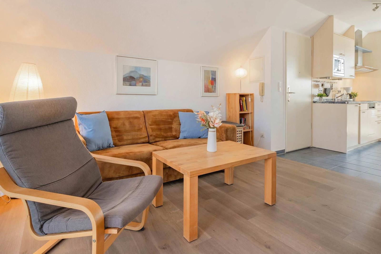 Wohnzimmer mit Sofa, Sessel und Esstisch. Küche im Hintergrund.
