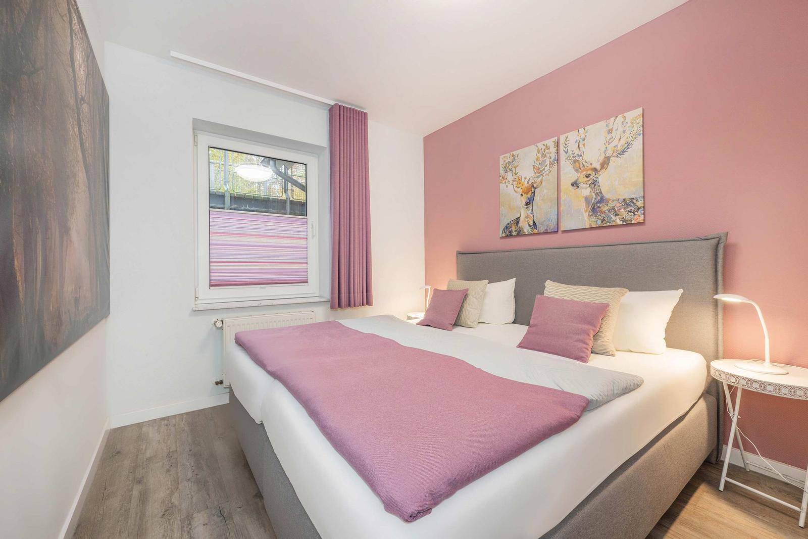 Schlafzimmer mit Bett, rosa Wand und Wandbildern von Hirschen.