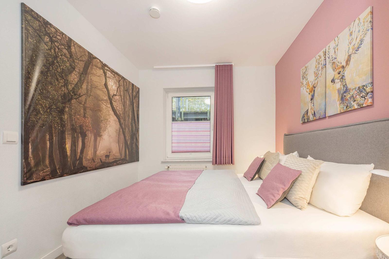 Schlafzimmer mit Bett, Fenster und Wandbildern.