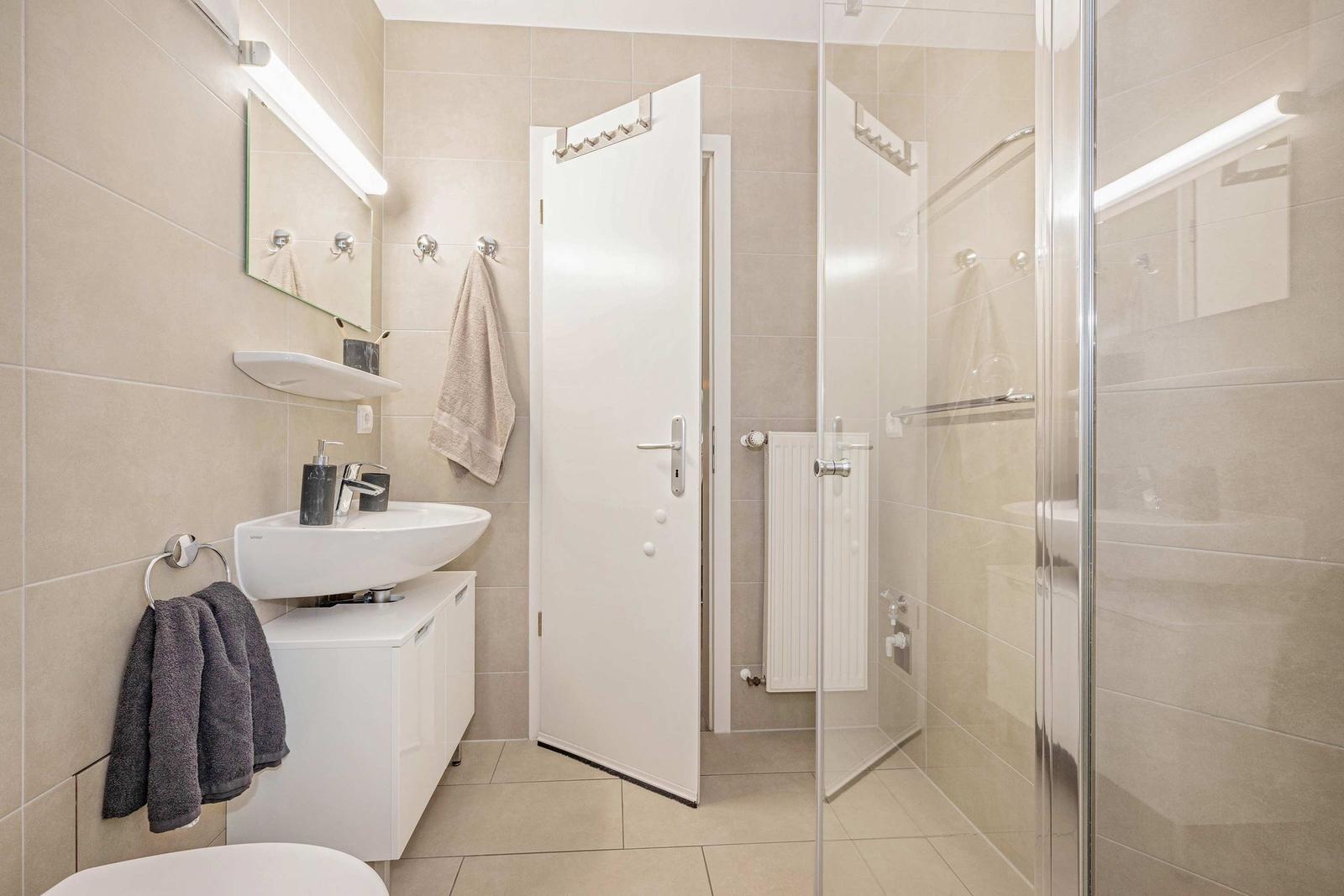 Badezimmer mit Dusche, Waschbecken und Toilette. Fliesenwand und weiße Möbel.