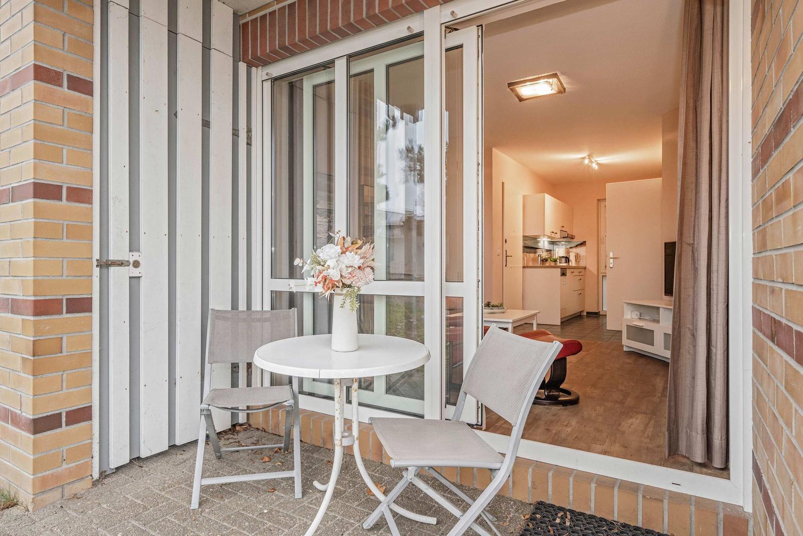 Terrasse mit Tisch und Stühlen. Durch Glastüren ist das Innere des Apartments sichtbar.