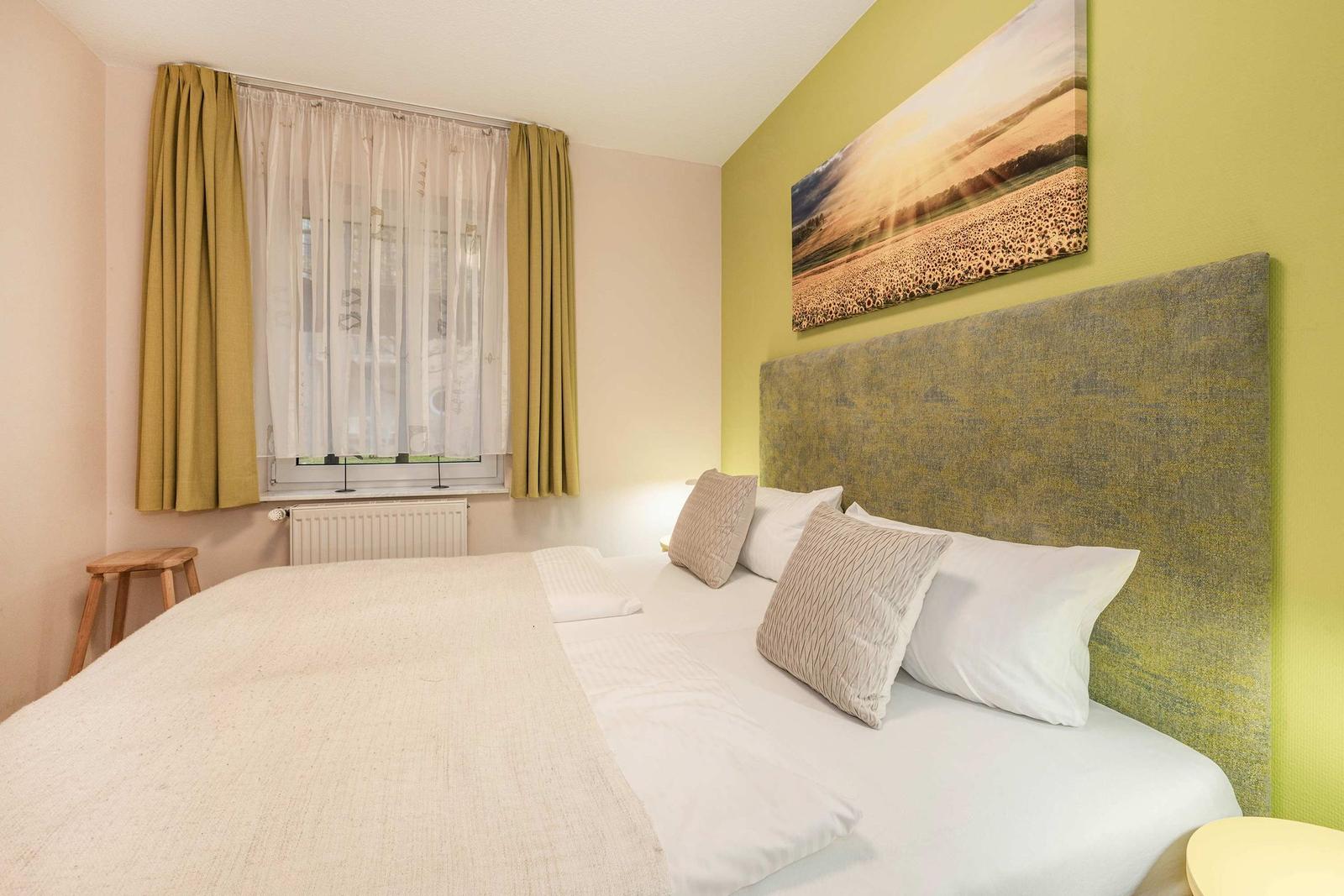 Schlafzimmer mit Bett, Fenster und Wandbild.
