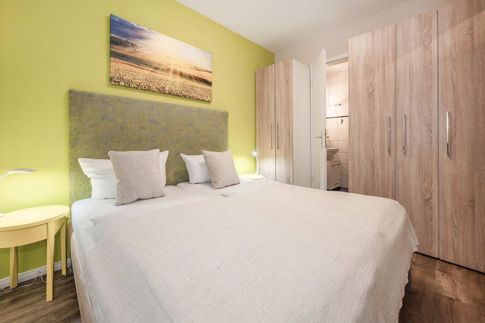 Schlafzimmer mit Doppelbett, Kleiderschrank und Wandbild. Badezimmer ist angebunden.