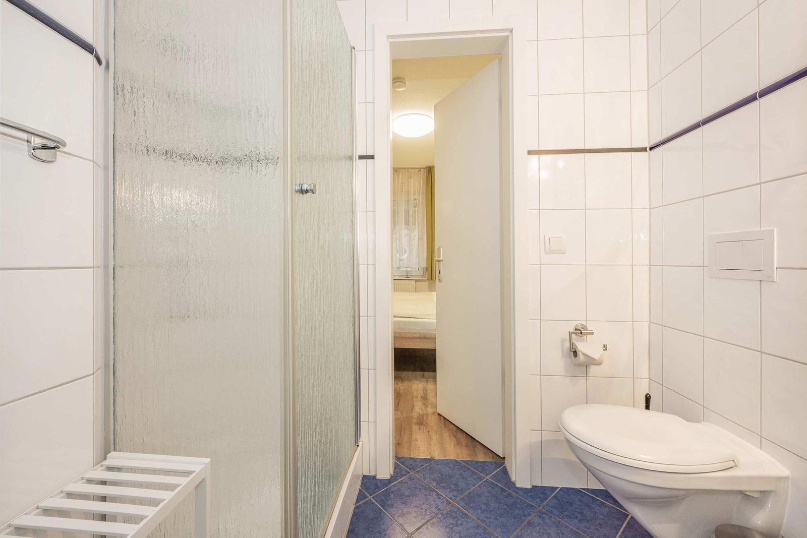 Badezimmer mit Dusche, Toilette und Blick in Schlafzimmer