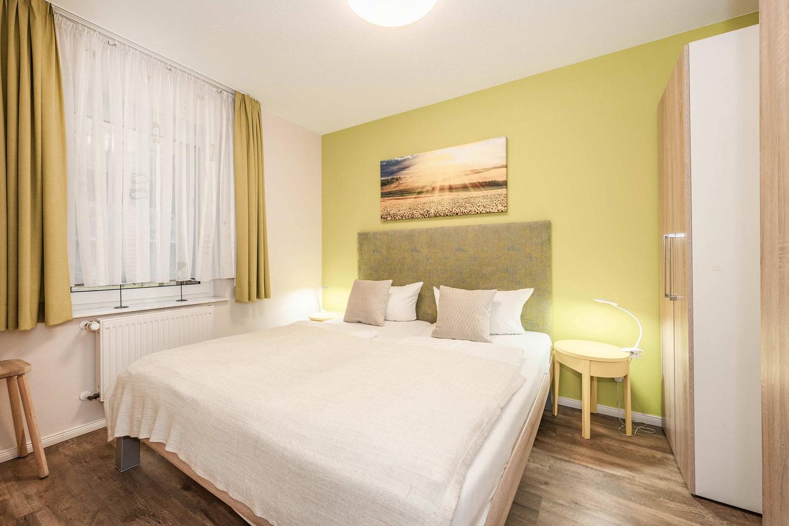 Schlafzimmer mit Bett, Wandbild und Gardinen.