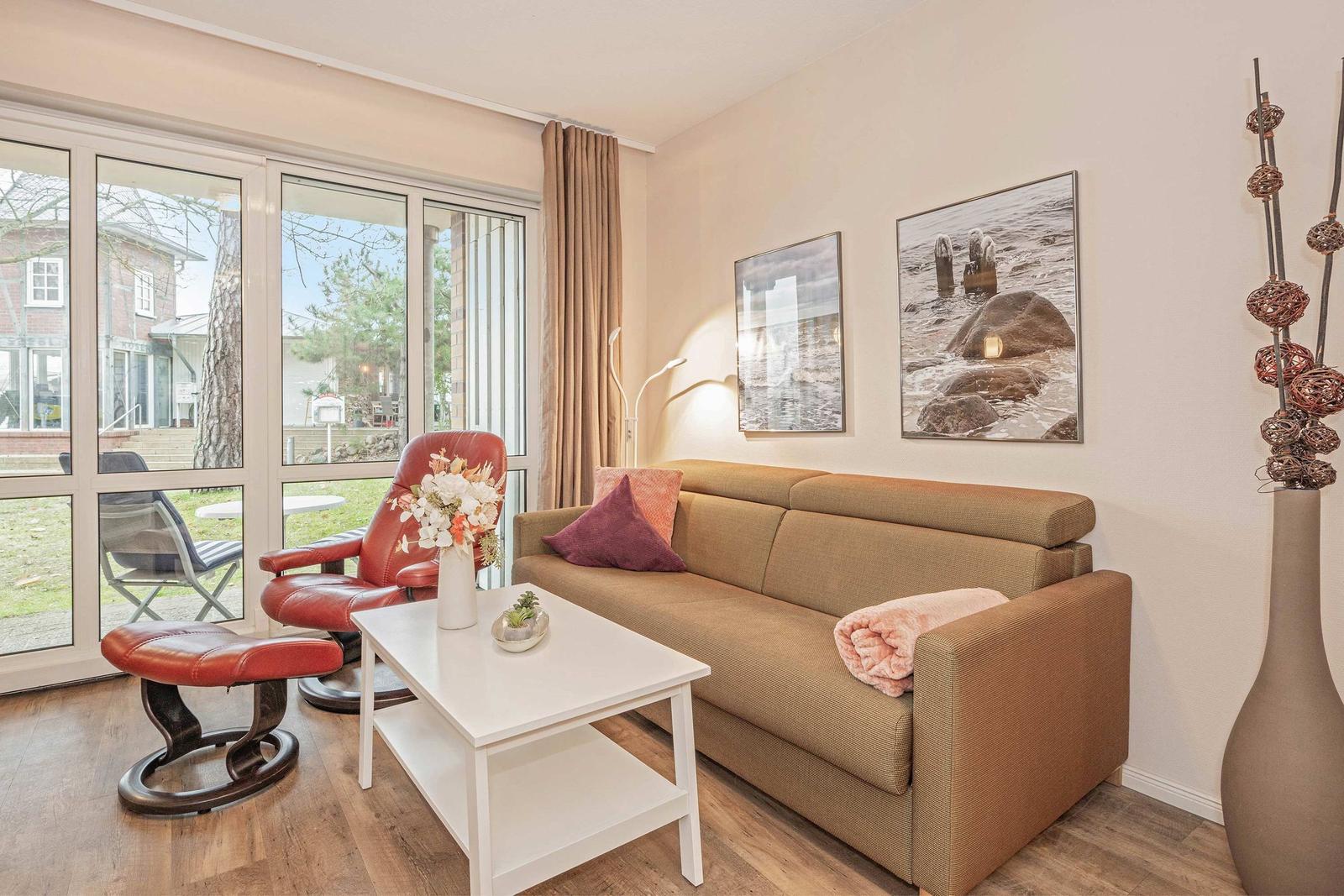 Wohnzimmer mit Sofa, Sessel und Fenster zum Garten